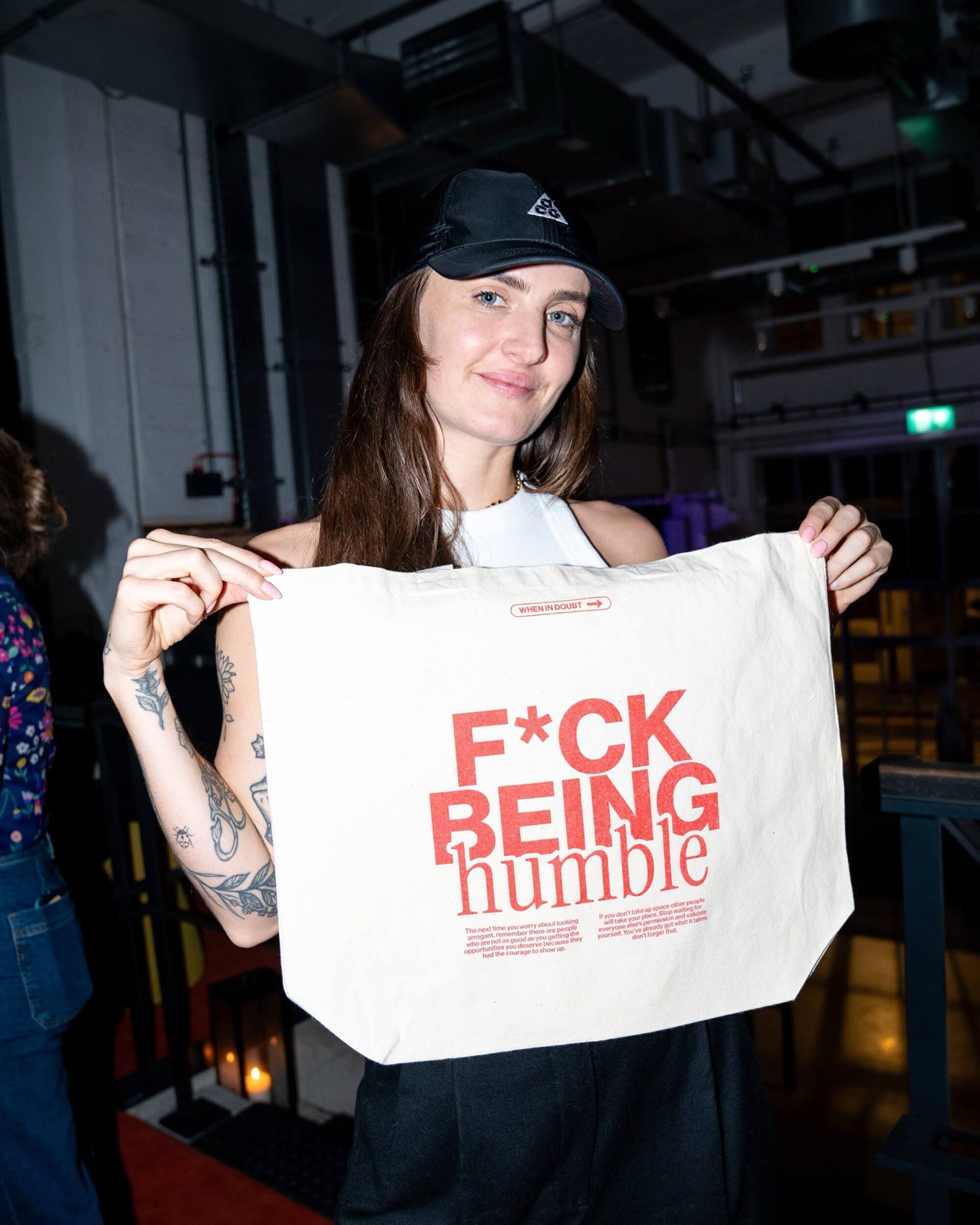 F*ck Being Humble tote bag held up in a dim setting