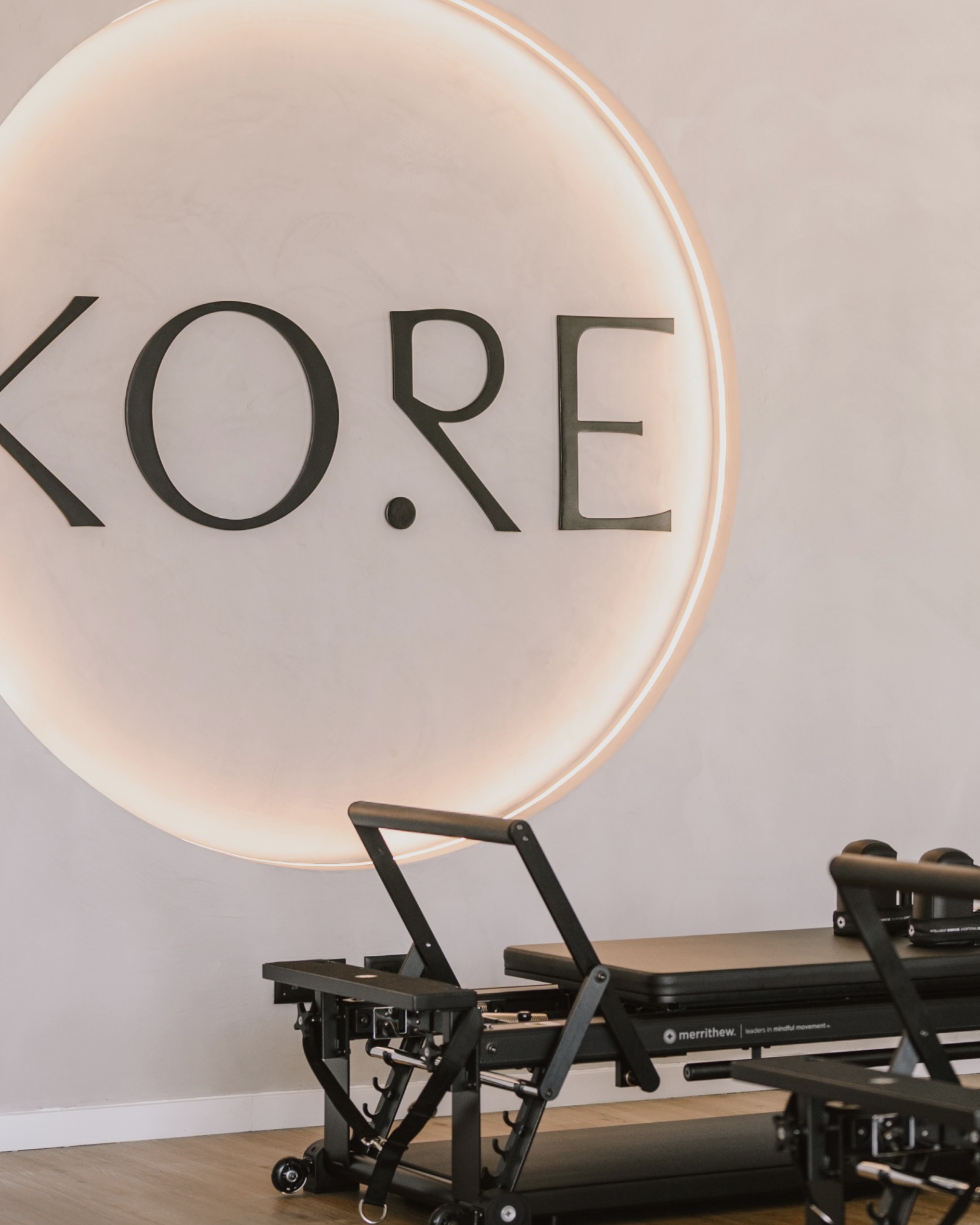 KORE logo lit on a circular wall sign above reformer machines in the Pilates studio