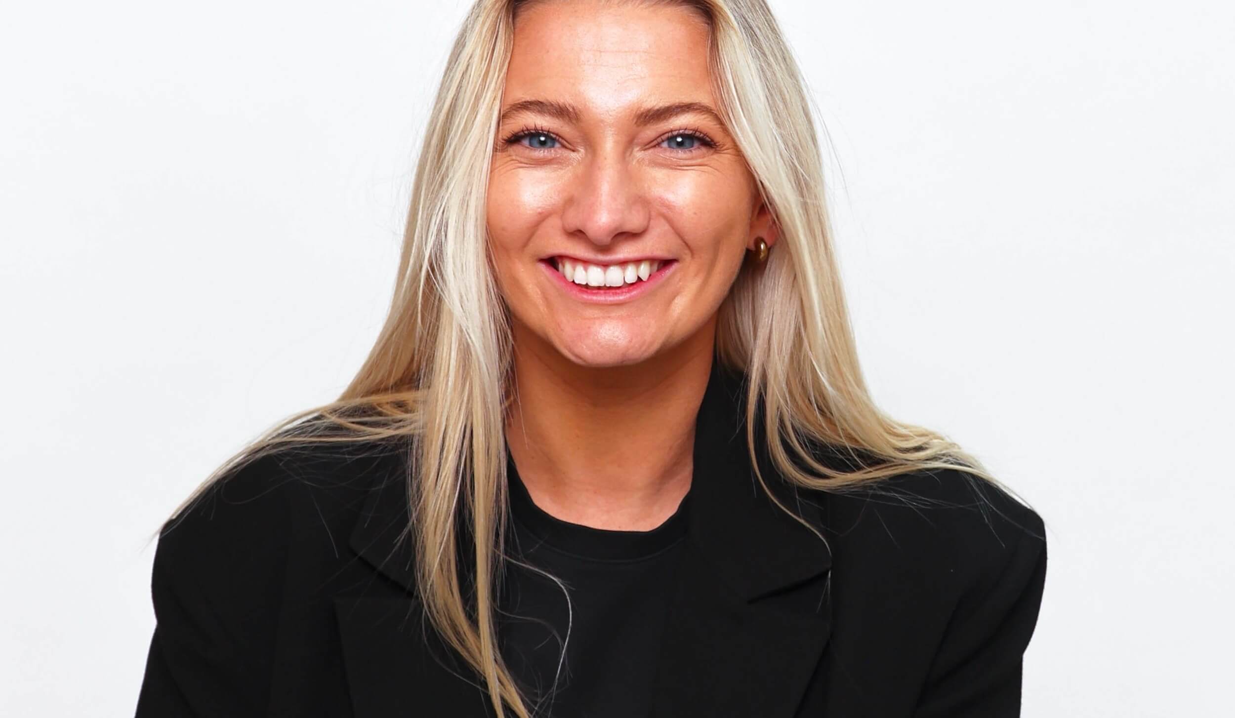 Alice Benham smiling in a black blazer against a white backdrop, from her personal brand photoshoot