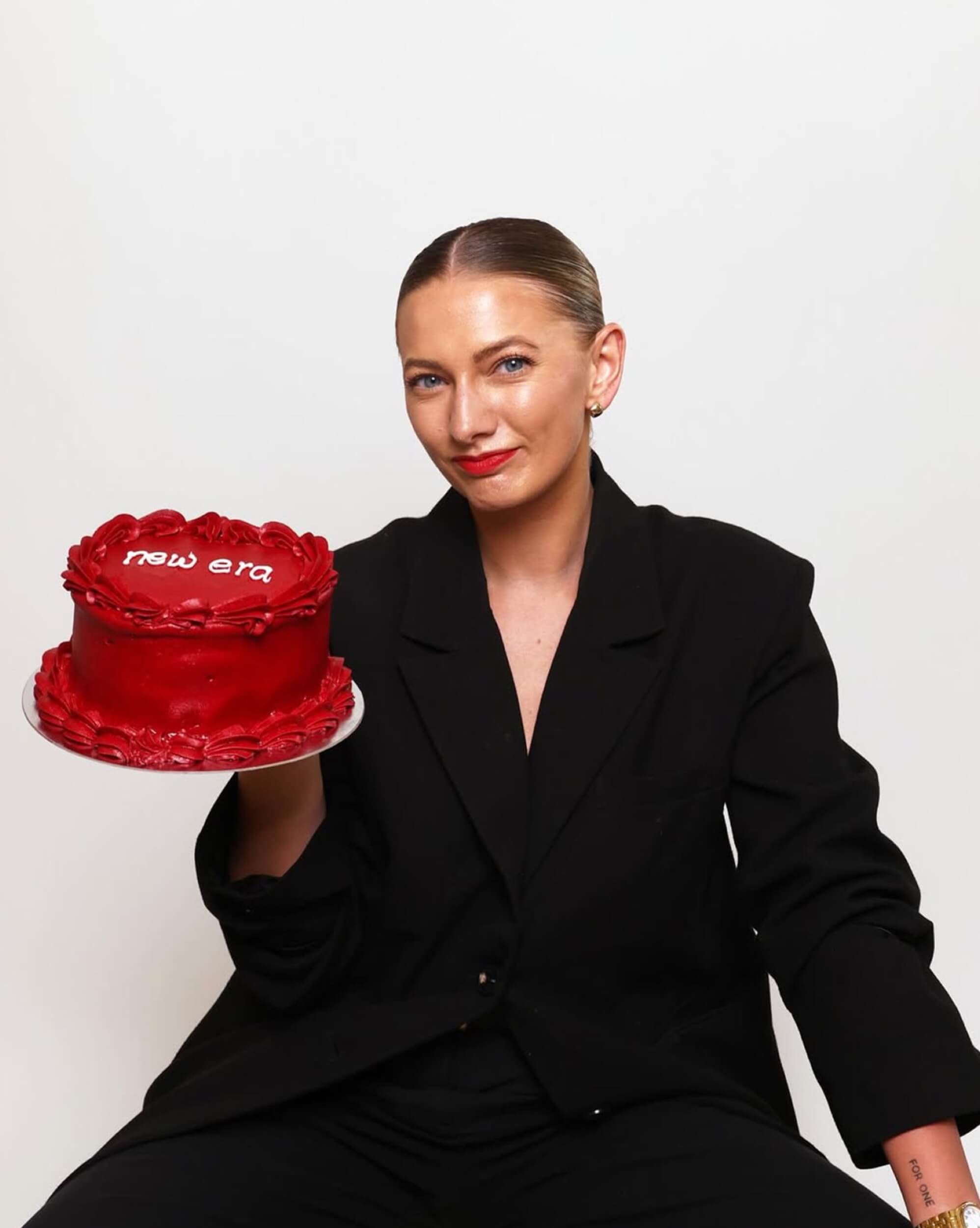 Alice Benham holding a red cake in a black suit, a playful shot from her personal brand photoshoot