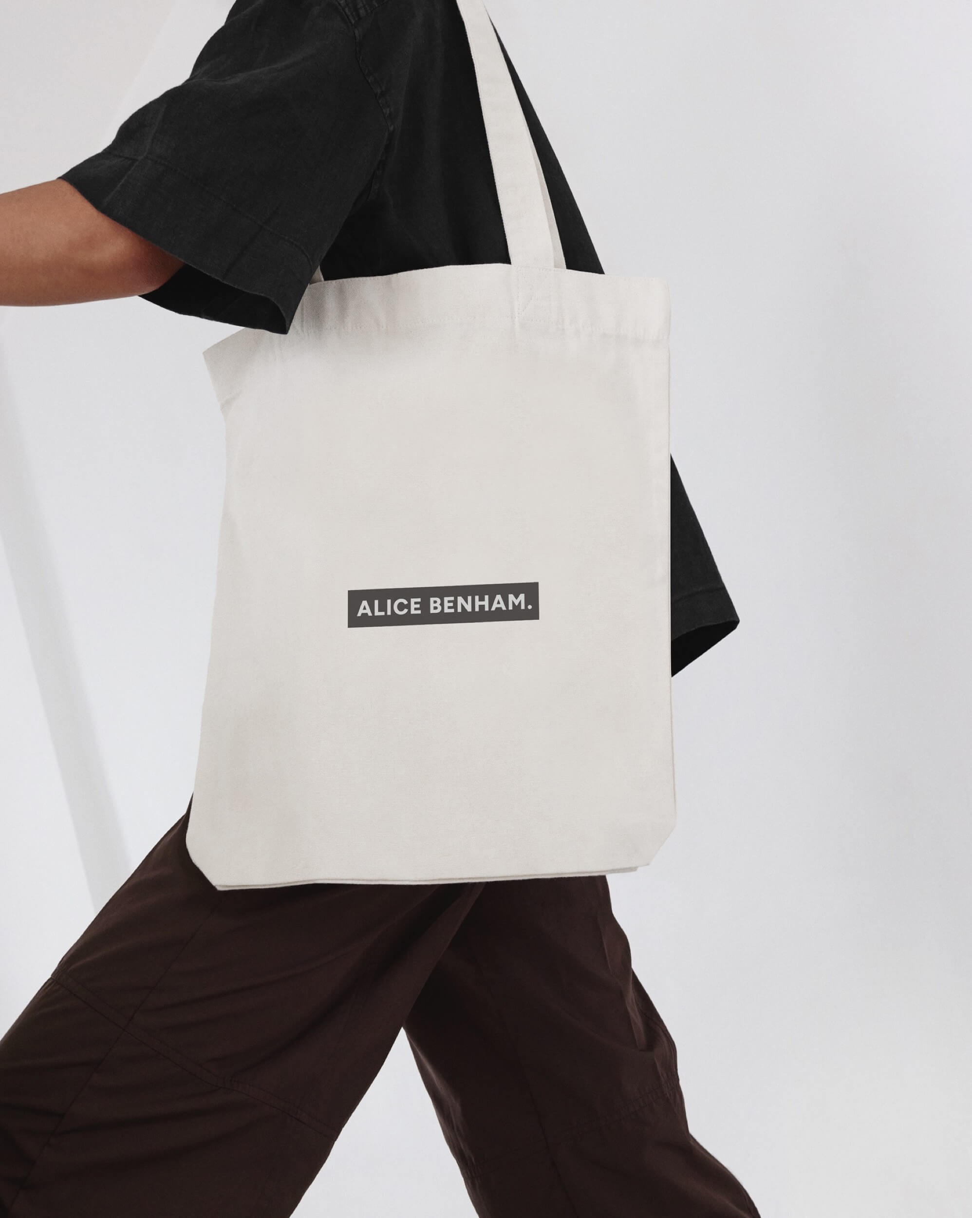 Alice Benham cream tote bag with her black wordmark label, carried against a light grey wall
