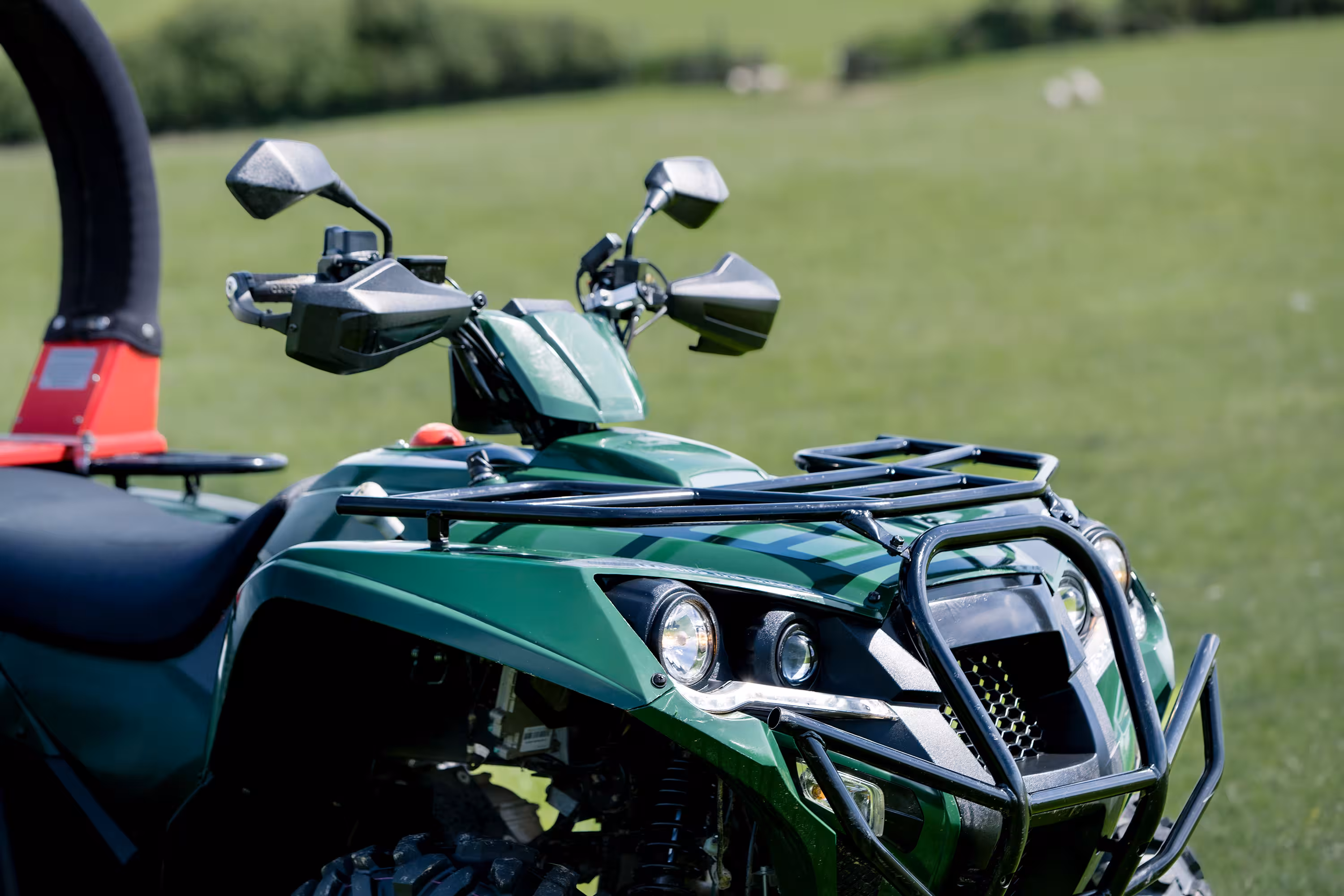 Close-up of green VoltQuad front with headlights, mirrors, and black protective rack on grass background.