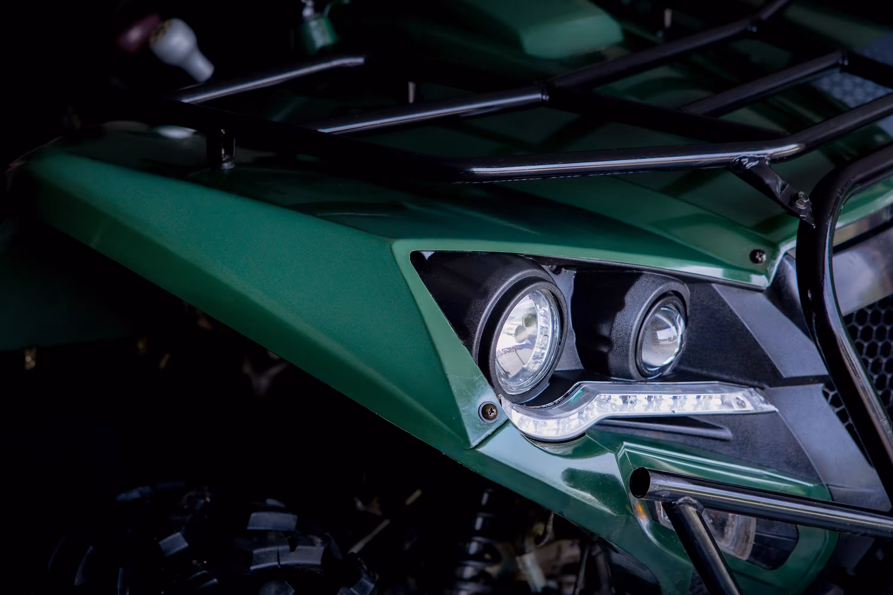 Front portion of a green VoltQuad vehicle showing headlights, guard bars, and a rugged tire.