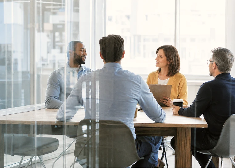 Quatre adultes assis autour d'une table dans une salle de réunion lumineuse et discutant.