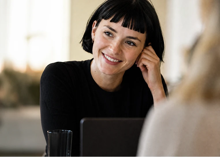 Jeune femme souriante aux cheveux noirs en conversation lors d'une réunion informelle.