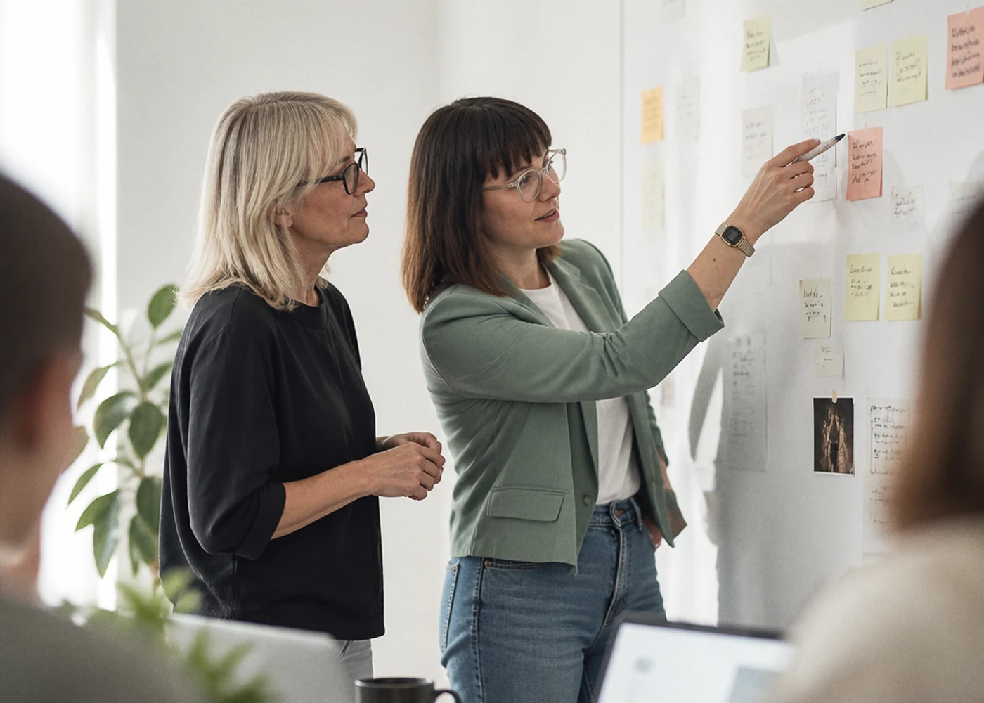 Deux femmes discutant devant un mur avec des notes autocollantes colorées dans un bureau lumineux.