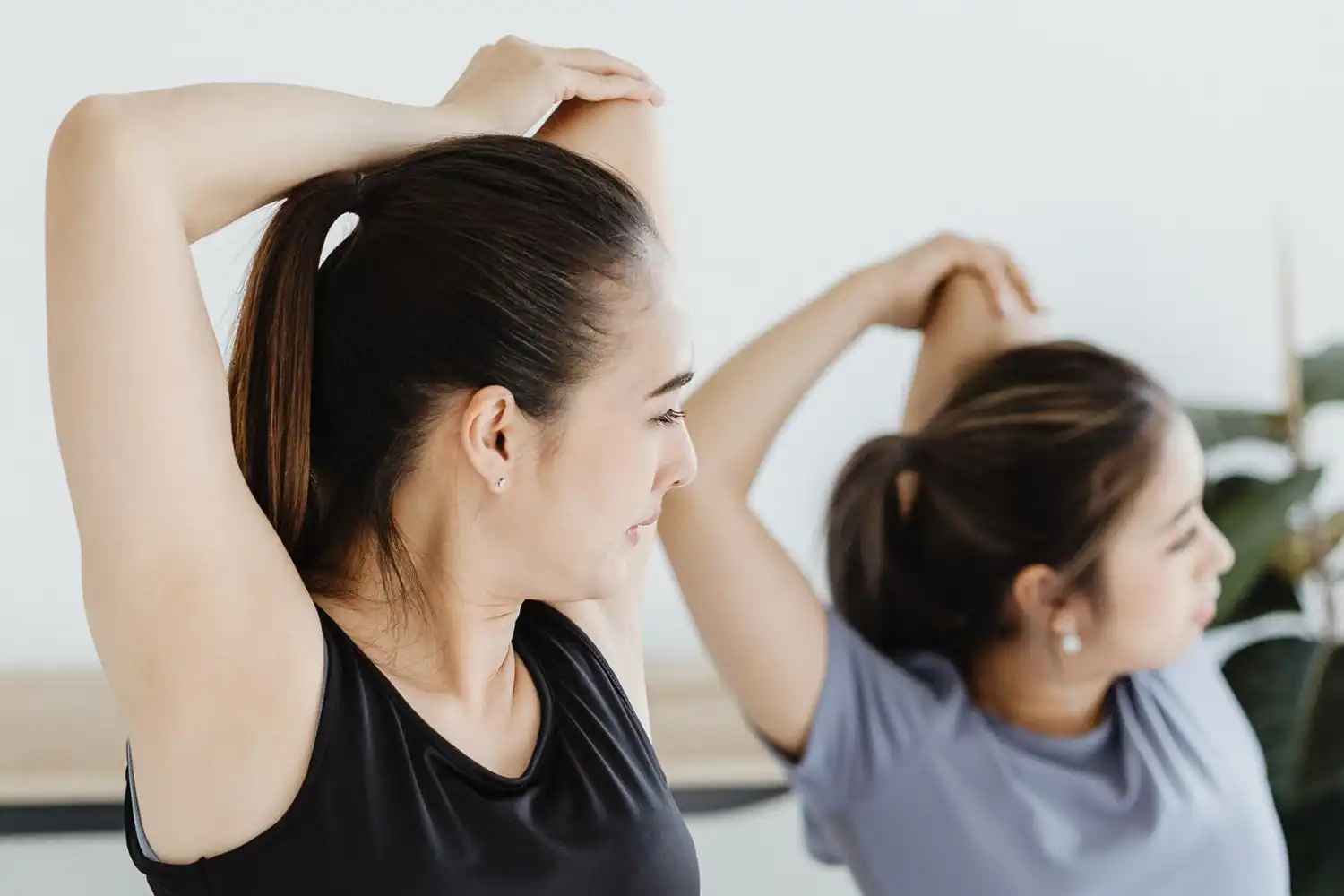 Deux femmes étirent bras au-dessus de la tête, exercice post-séance sport.