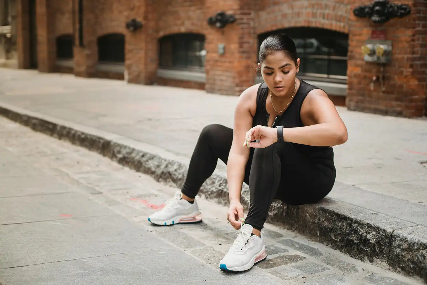 Femme ajustant lacet basket lors d’une pause sport en extérieur près d’un bâtiment industriel