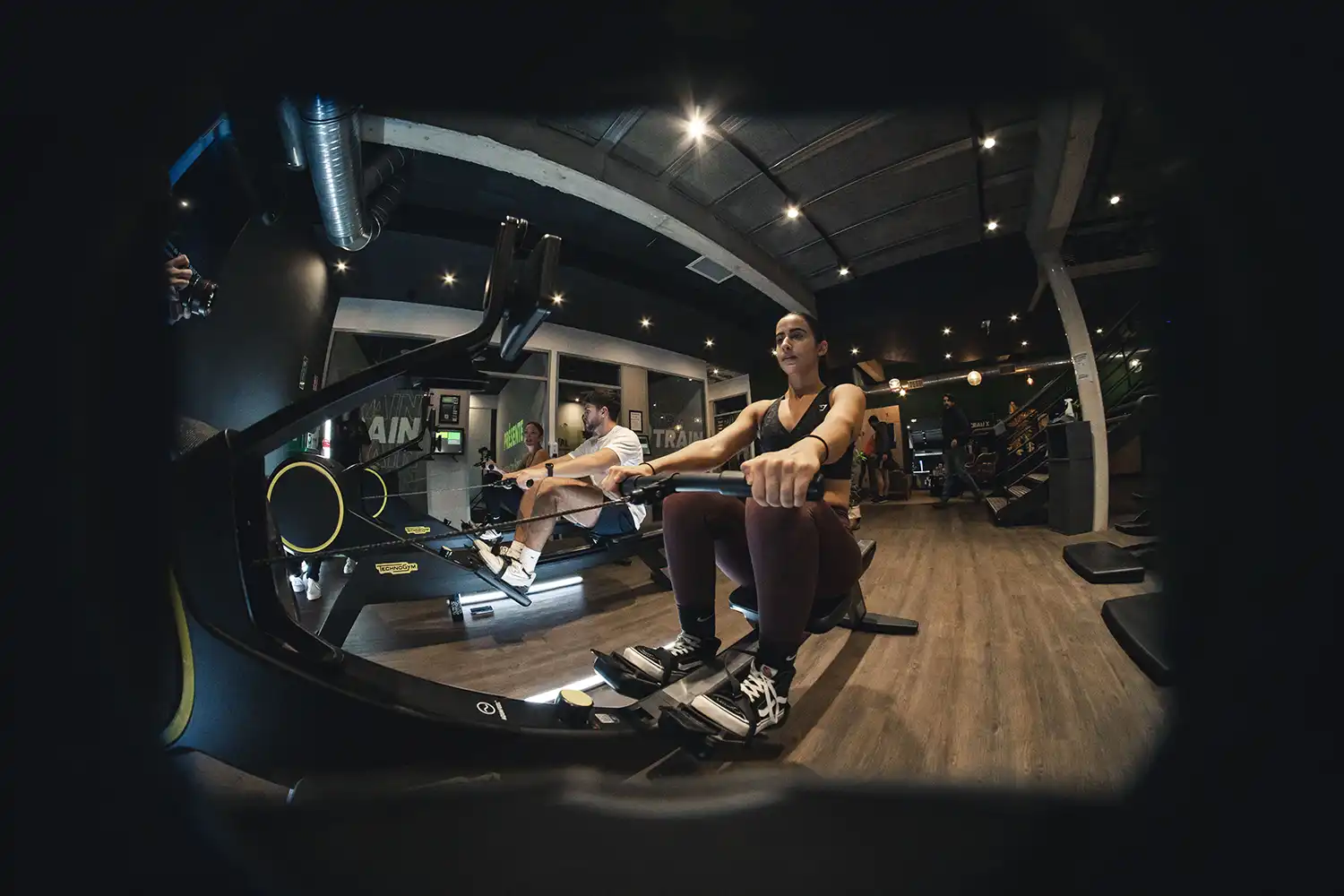 Salle de sport Keepcool, deux personnes utilisant des vélos elliptiques cardio-training en intérieur moderne.