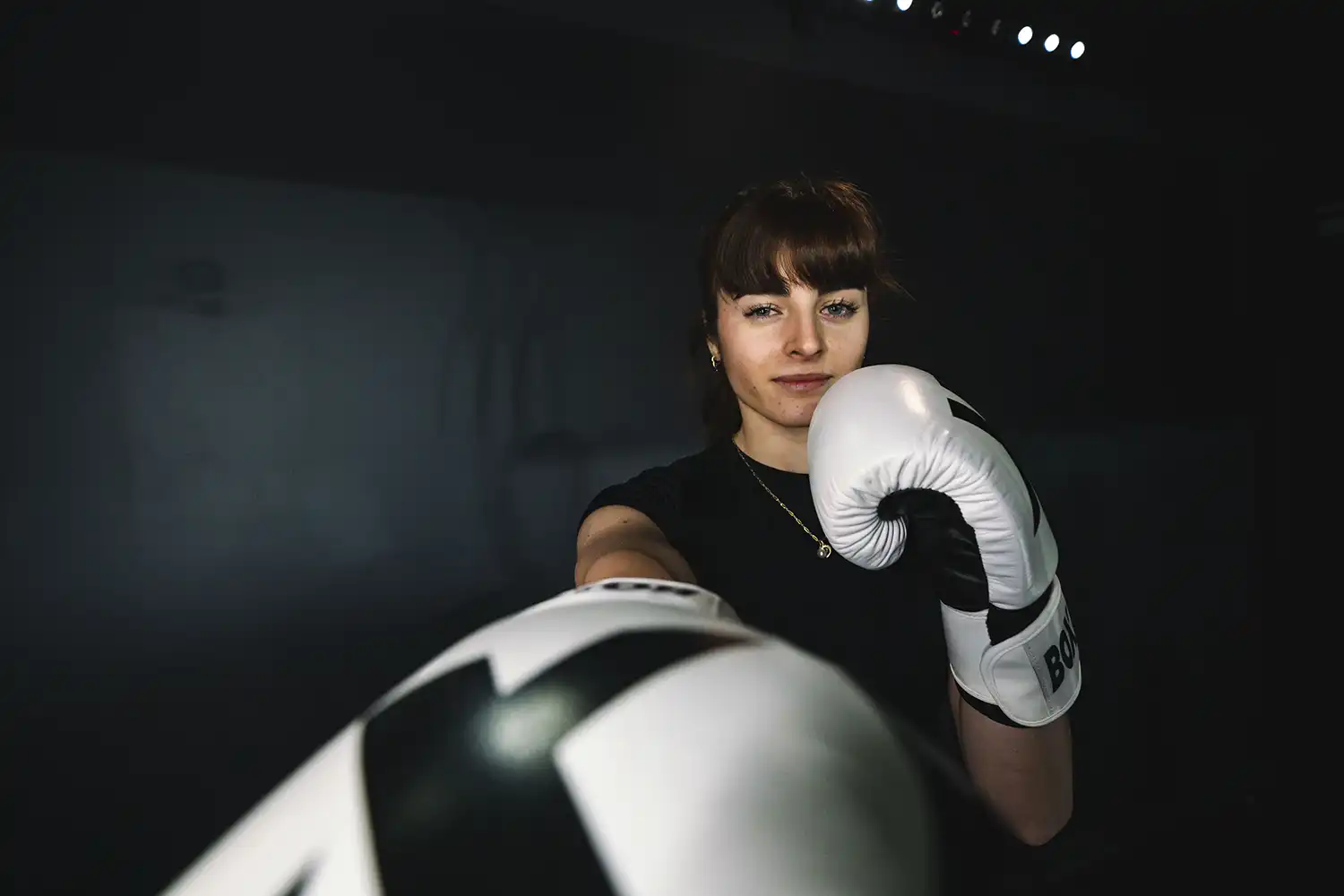 Personne en salle de sport tenant gants de boxe, posture de combat, environnement sportif Keepcool