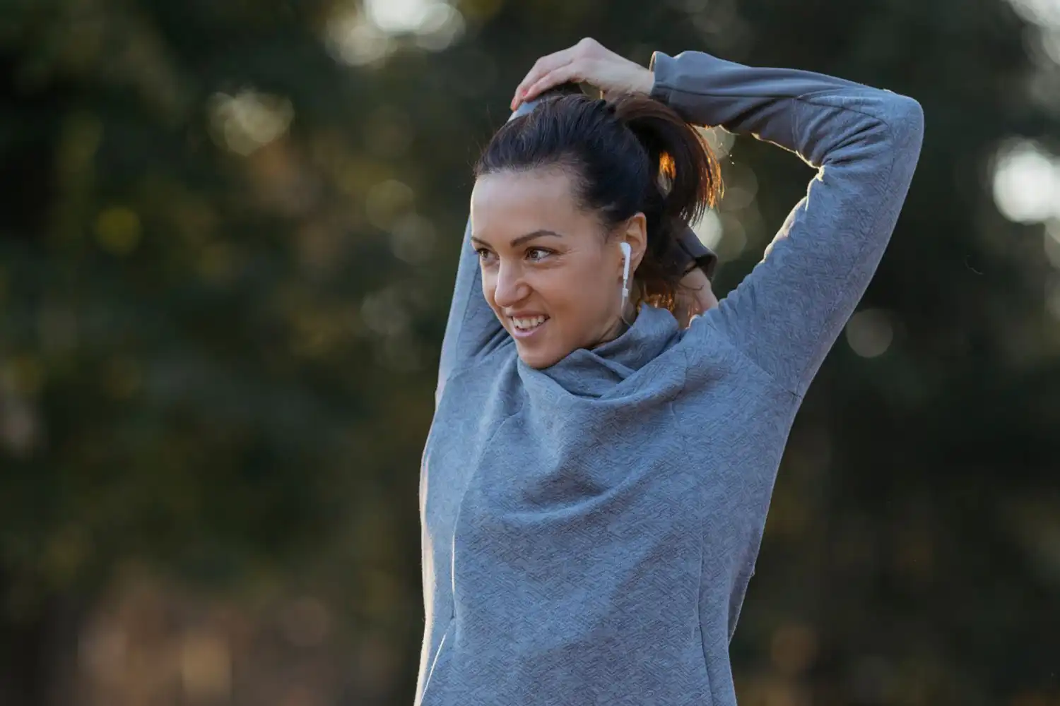 Femme s’étire les bras avec écouteurs, activité fitness en extérieur