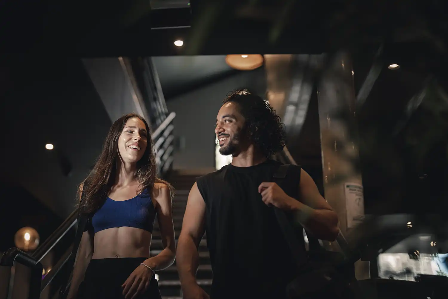 Deux sportifs souriants en salle de sport moderne, participant à un cours collectif dynamique.