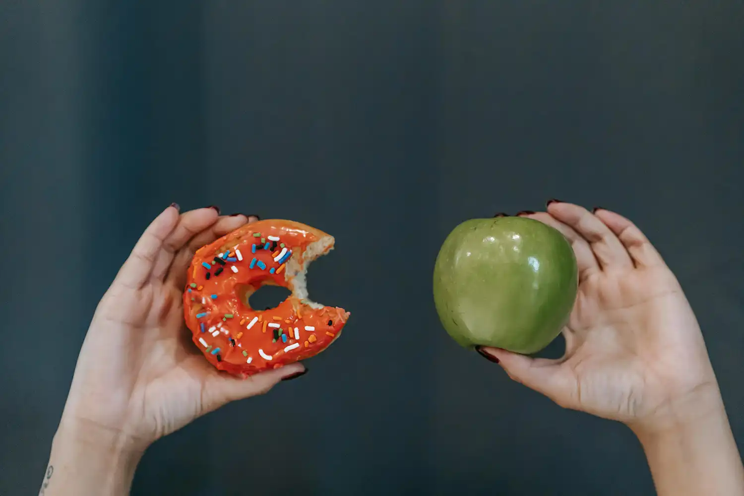Mains tenant un donut sucré et une pomme verte, choix alimentaire équilibré