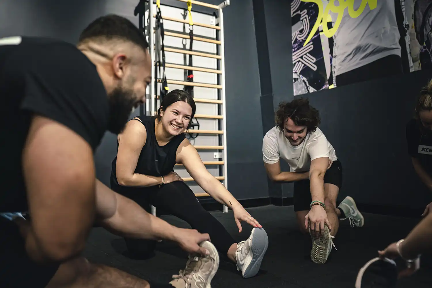 Trois personnes s'étirent dans une salle de sport moderne après une séance de sport.