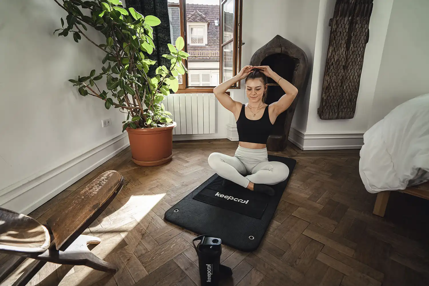 Femme pratiquant yoga sur tapis Keepcool en intérieur, posture d’étirement dynamique près d’une fenêtre.