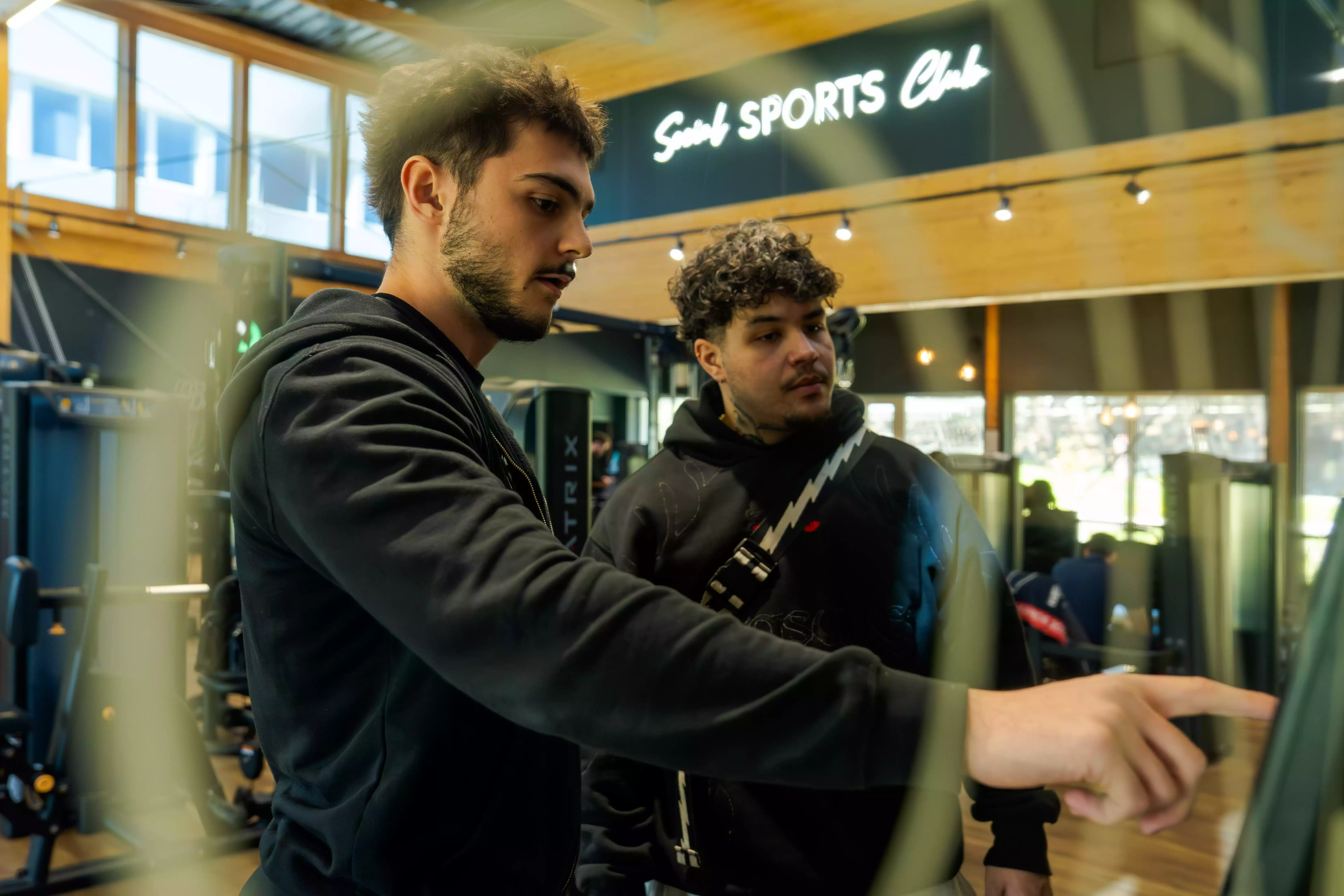 Deux hommes discutent près d’un comptoir dans un club Keepcool Sports Club, environnement moderne et accueillant pour sportifs.