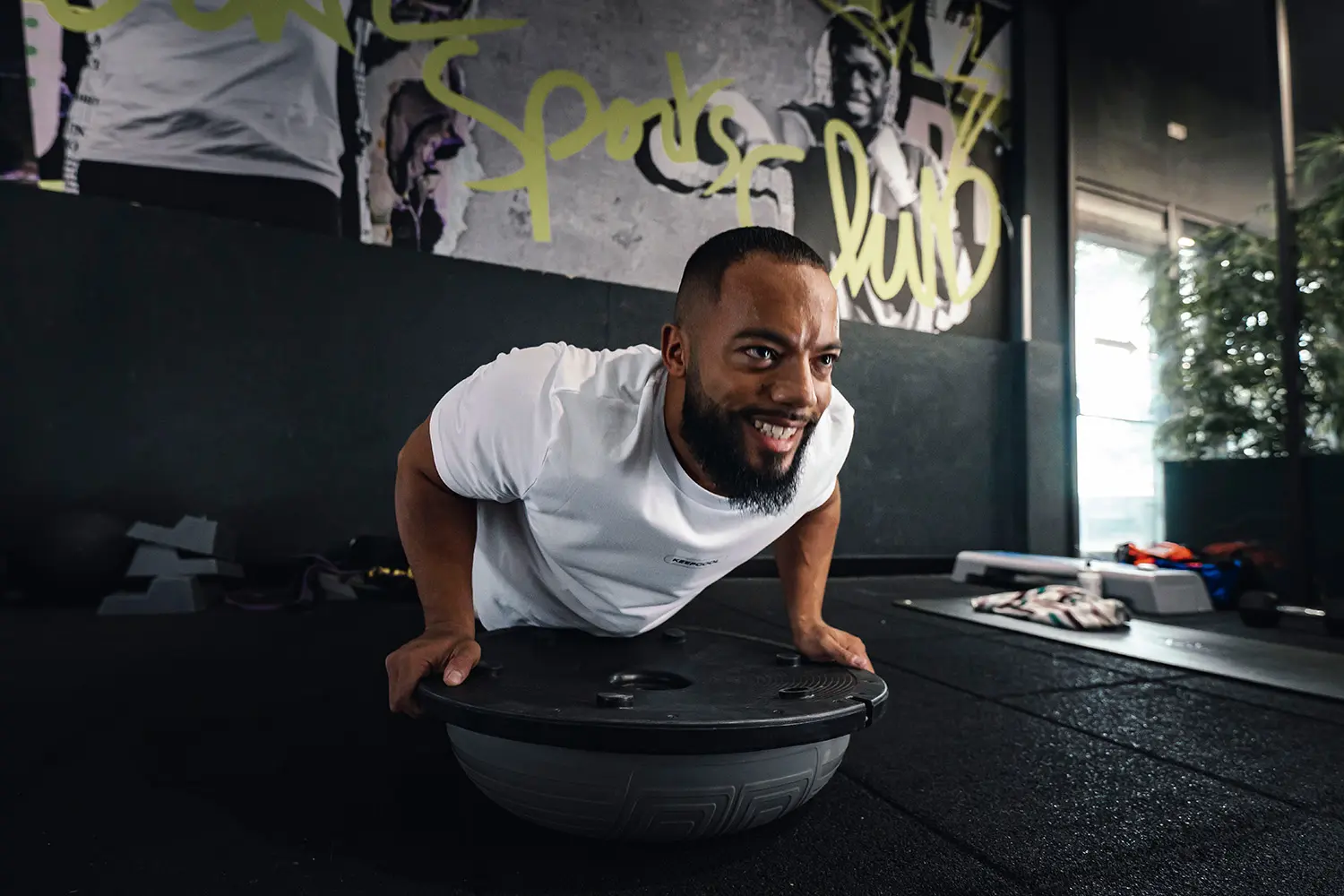 Homme souriant en exercice sur ballon de gym en salle de sport moderne