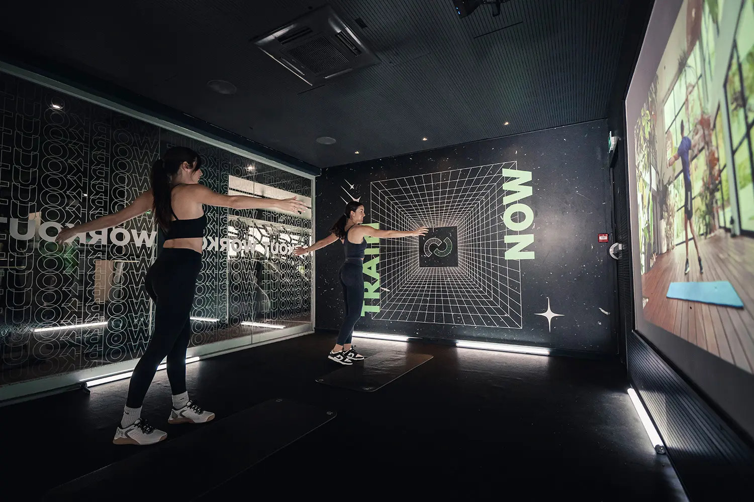 Deux personnes en salle de sport Keepcool participant à un cours collectif devant écrans interactifs pour entraînement cardio et musculation