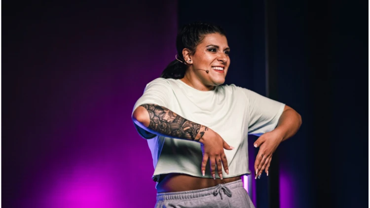 Femme souriante en tenue décontractée, pose dynamique sur scène, cours collectifs sportifs.