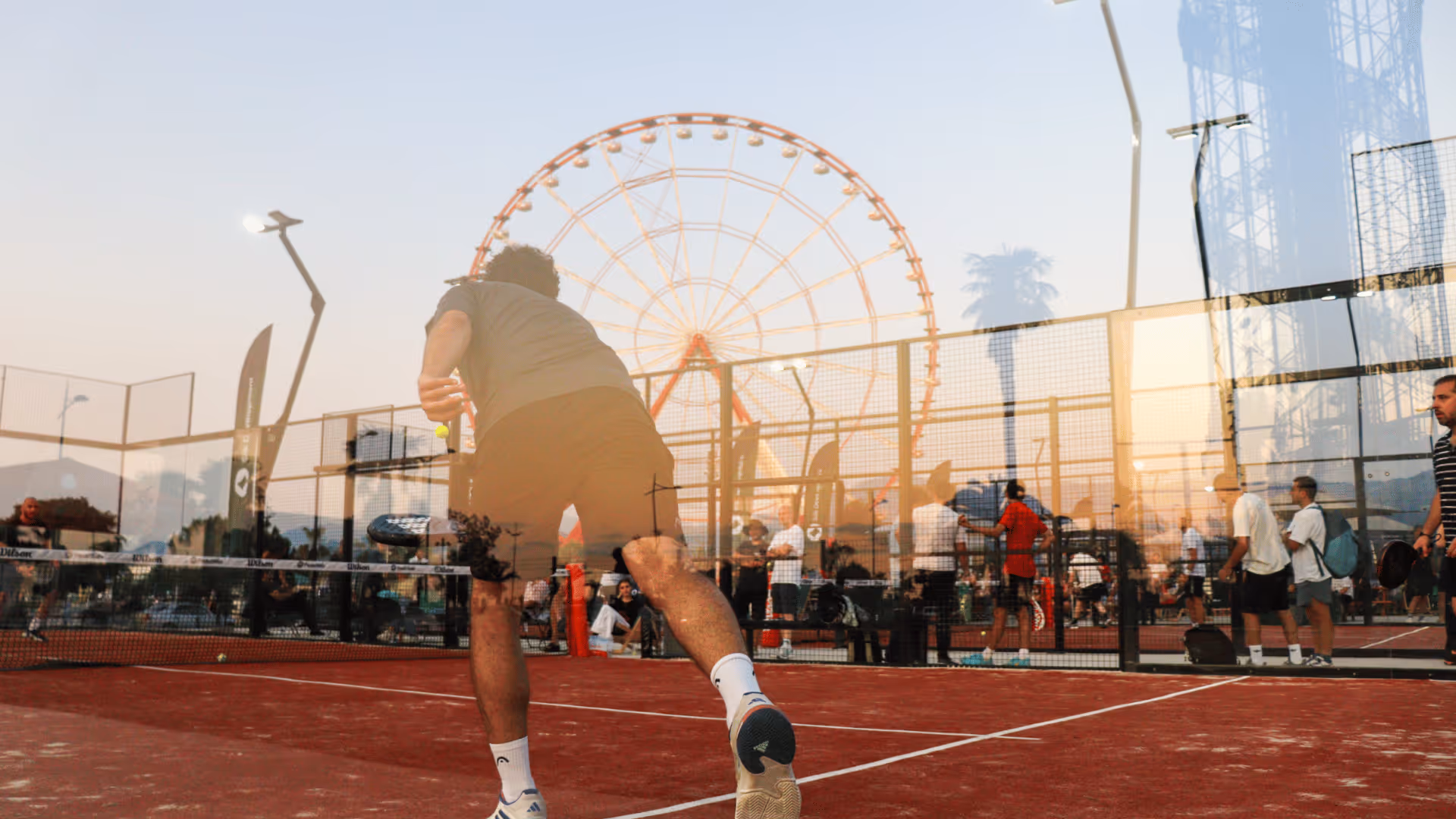 Padel Port - located in georgia, batumi. A guy playing padel on a red court, in the glass there is a reflection of a panoramic wheel. 
