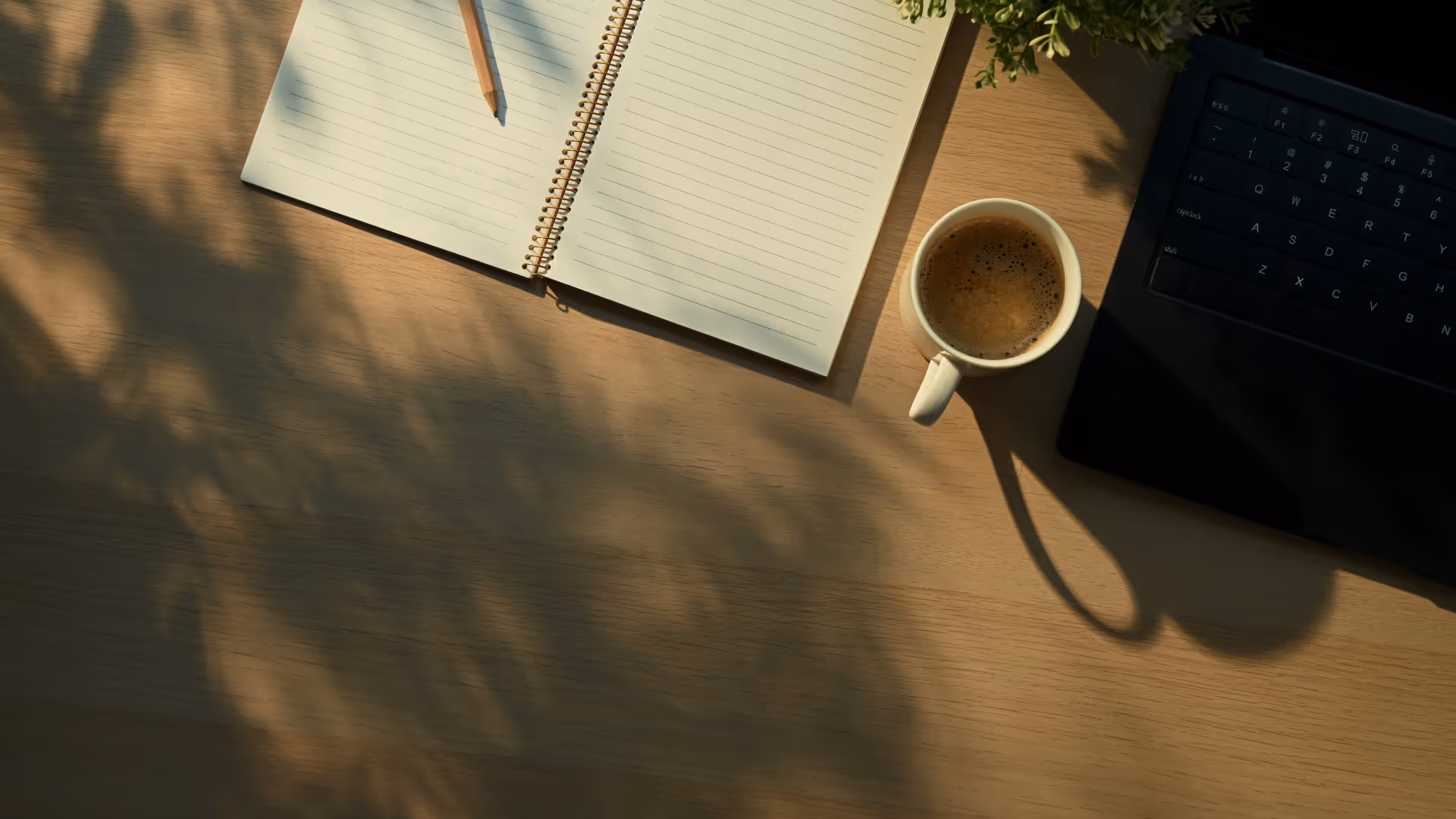 Wooden desk with open lined notebook, pencil, cup of coffee, and partially visible laptop keyboard.