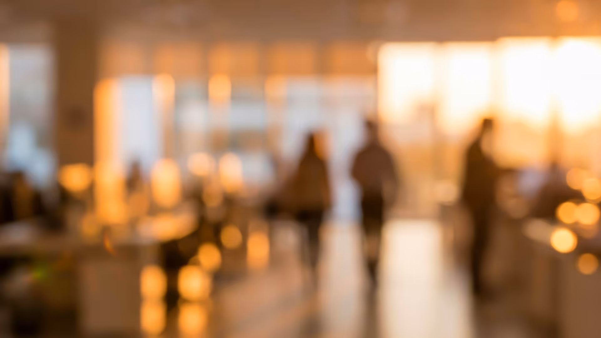 Blurred view of people walking in a sunlit office space with warm lighting.