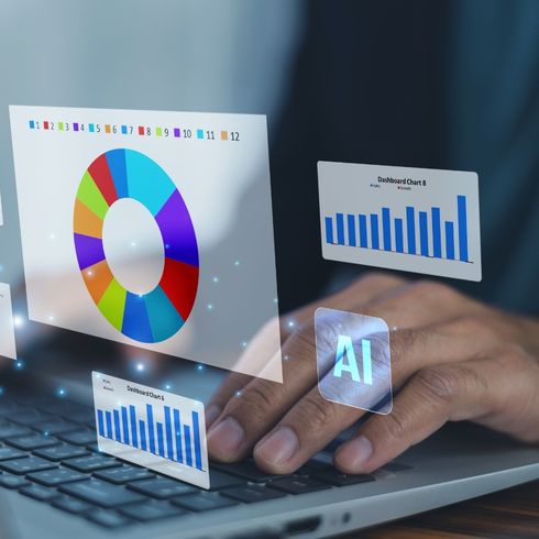 Hand typing on laptop with holographic AI symbol and colorful data charts floating above keyboard.