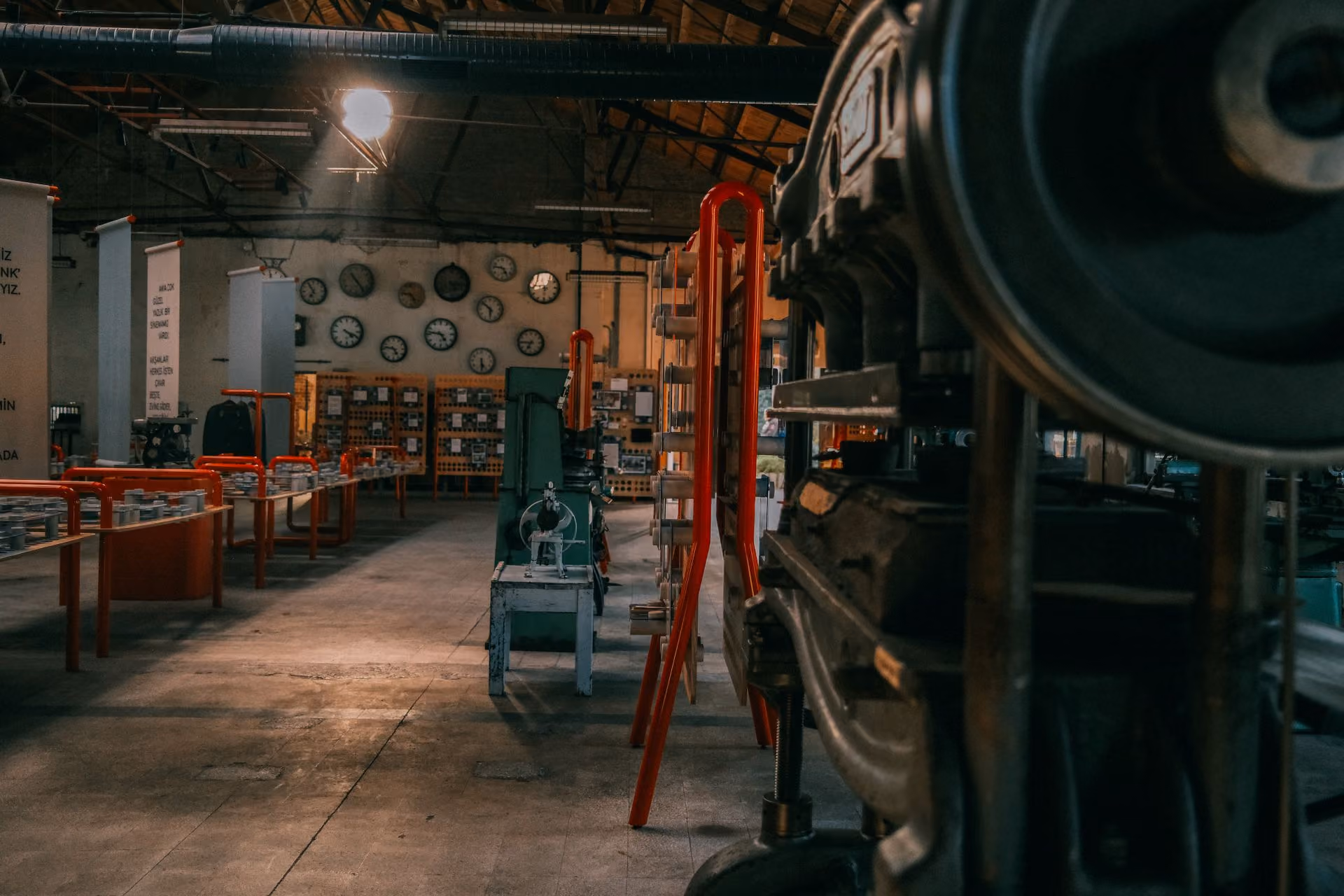 Interior of an industrial workshop with clocks on the wall and machinery along the room sides.