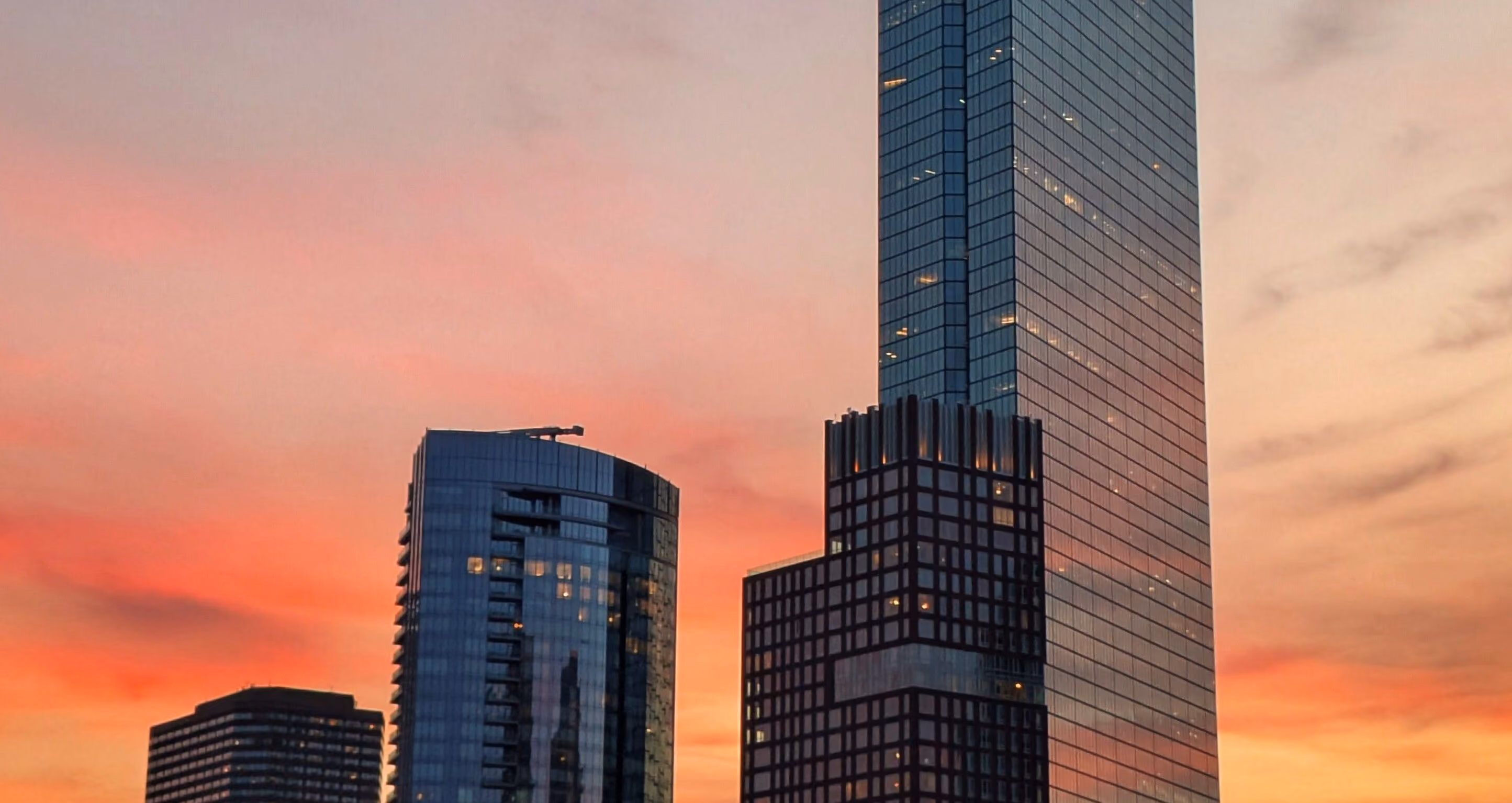 Modern skyscrapers with glass facades at sunset under a colorful pink and orange sky.
