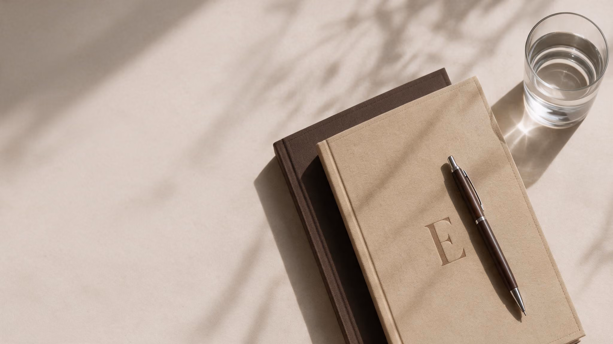 A top view image of table with a glass on top of it and book and pen.