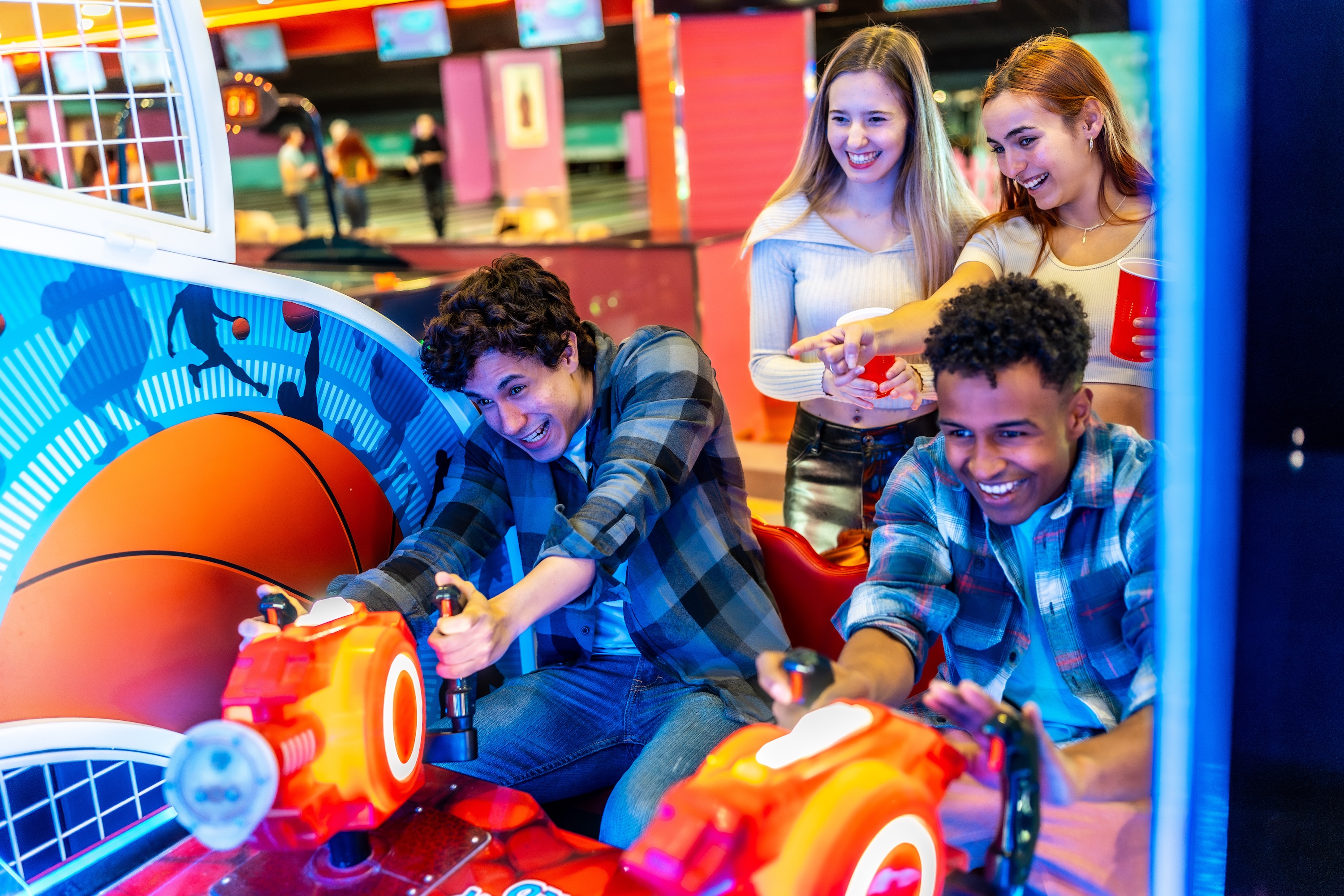 Friends playing arcade basketball game together in bowling alley stock image