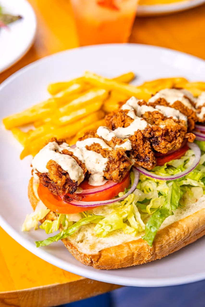 A sandwich with lettuce, tomato, and fries on a white plate.
