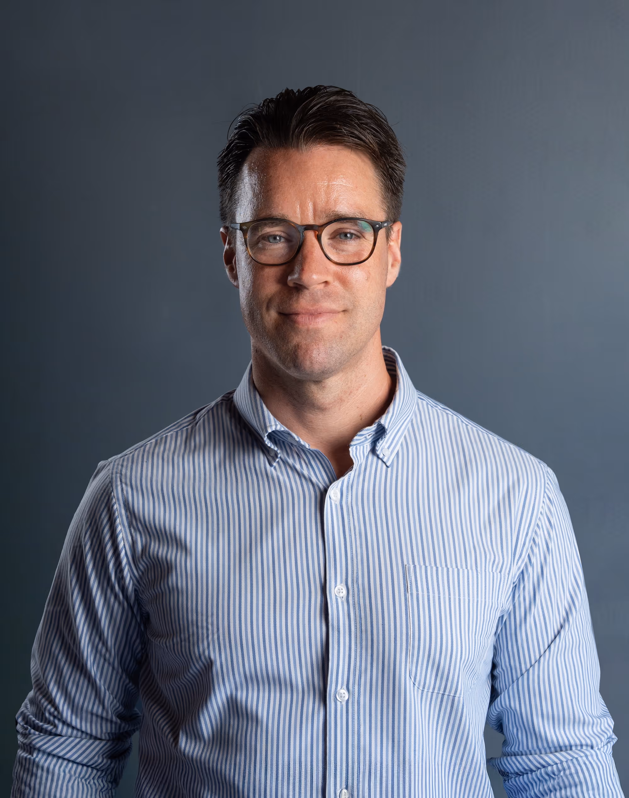 Man with short brown hair and glasses wearing a blue and white striped button-up shirt.