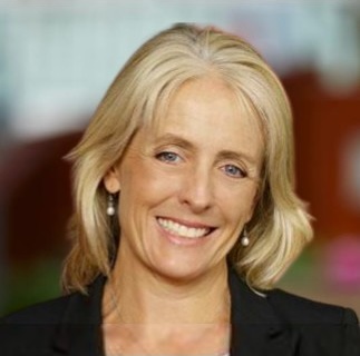 Smiling middle-aged woman with blonde hair wearing pearl earrings and a black jacket.