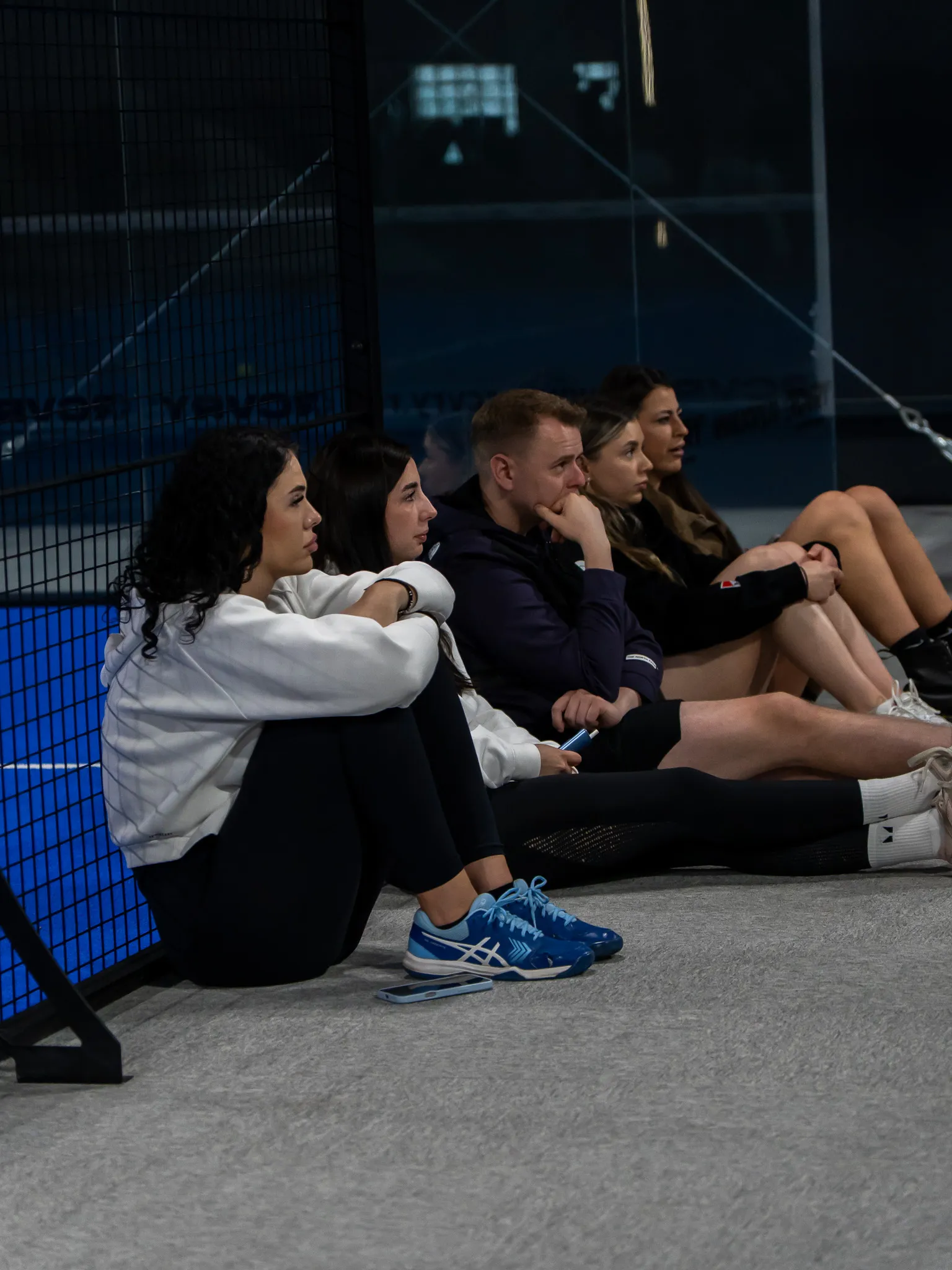 Prieteni din comunitatea PADELMANIA care urmăresc un meci, așezați lângă teren