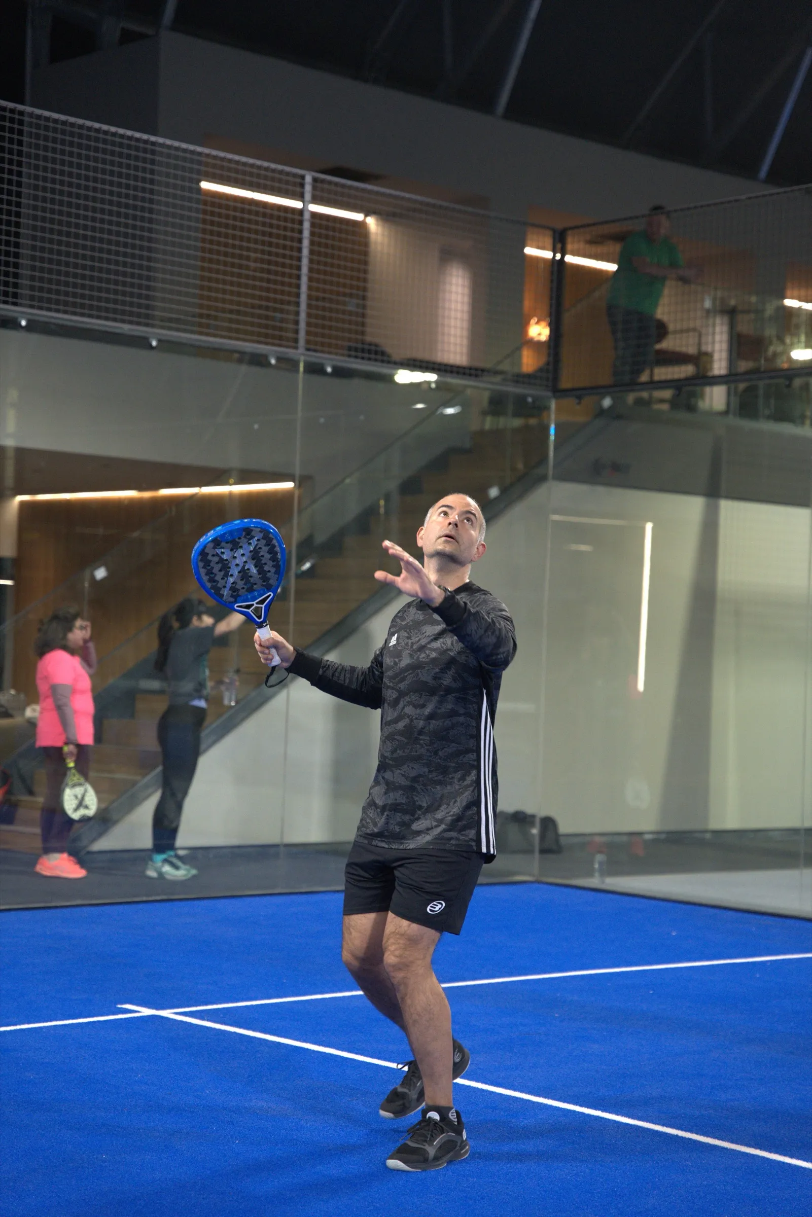 Jucător pregătește un smash pe un teren indoor, cu lounge-ul de la etaj în fundal, la PADELMANIA Tunari