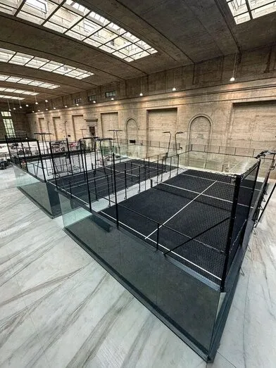 Terenuri de padel Full Panoramic cu pereți de sticlă și gazon negru, într-o hală cu luminatoare