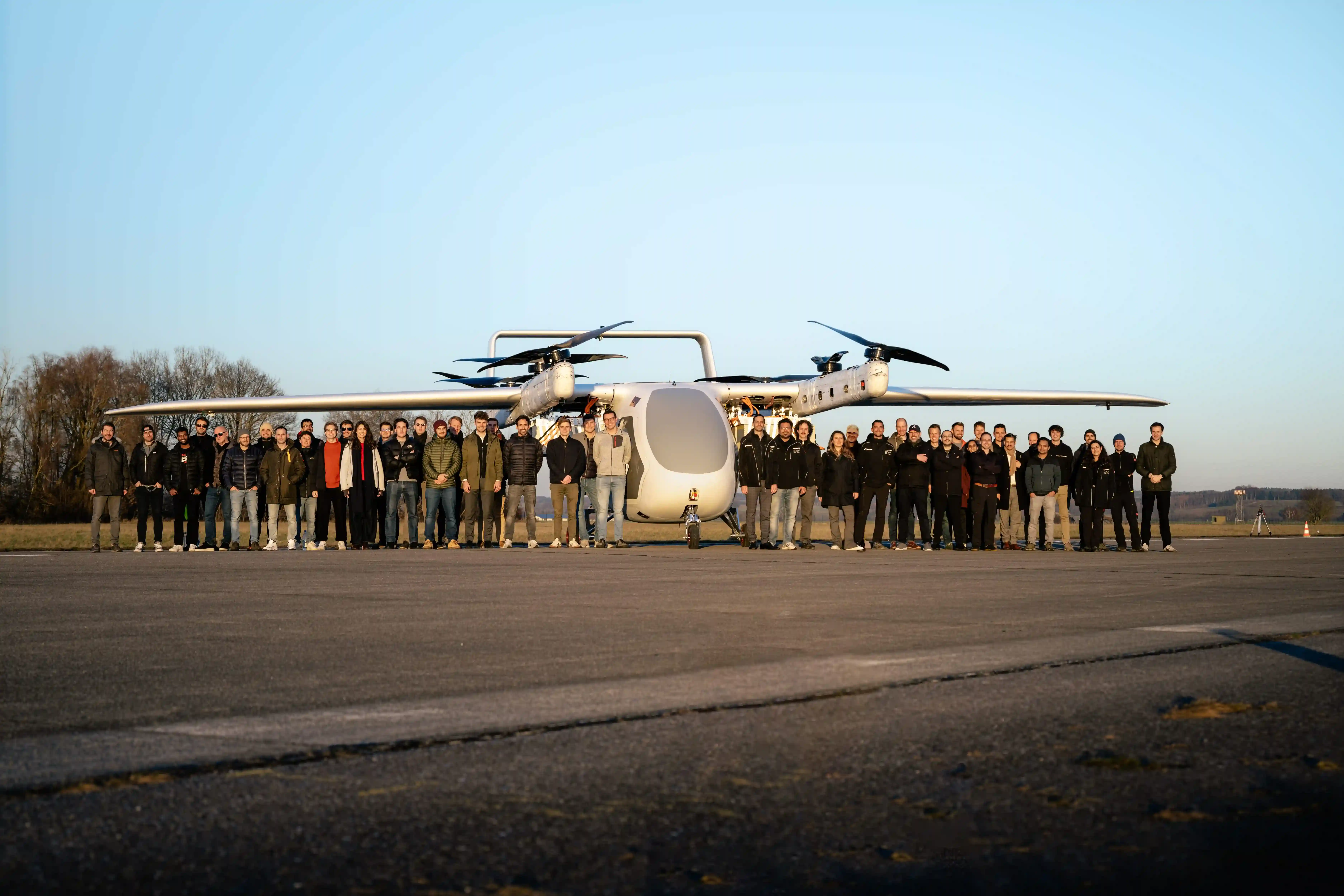 Group of people standing in front of a large white aircraft with four visible propellers on a runway.