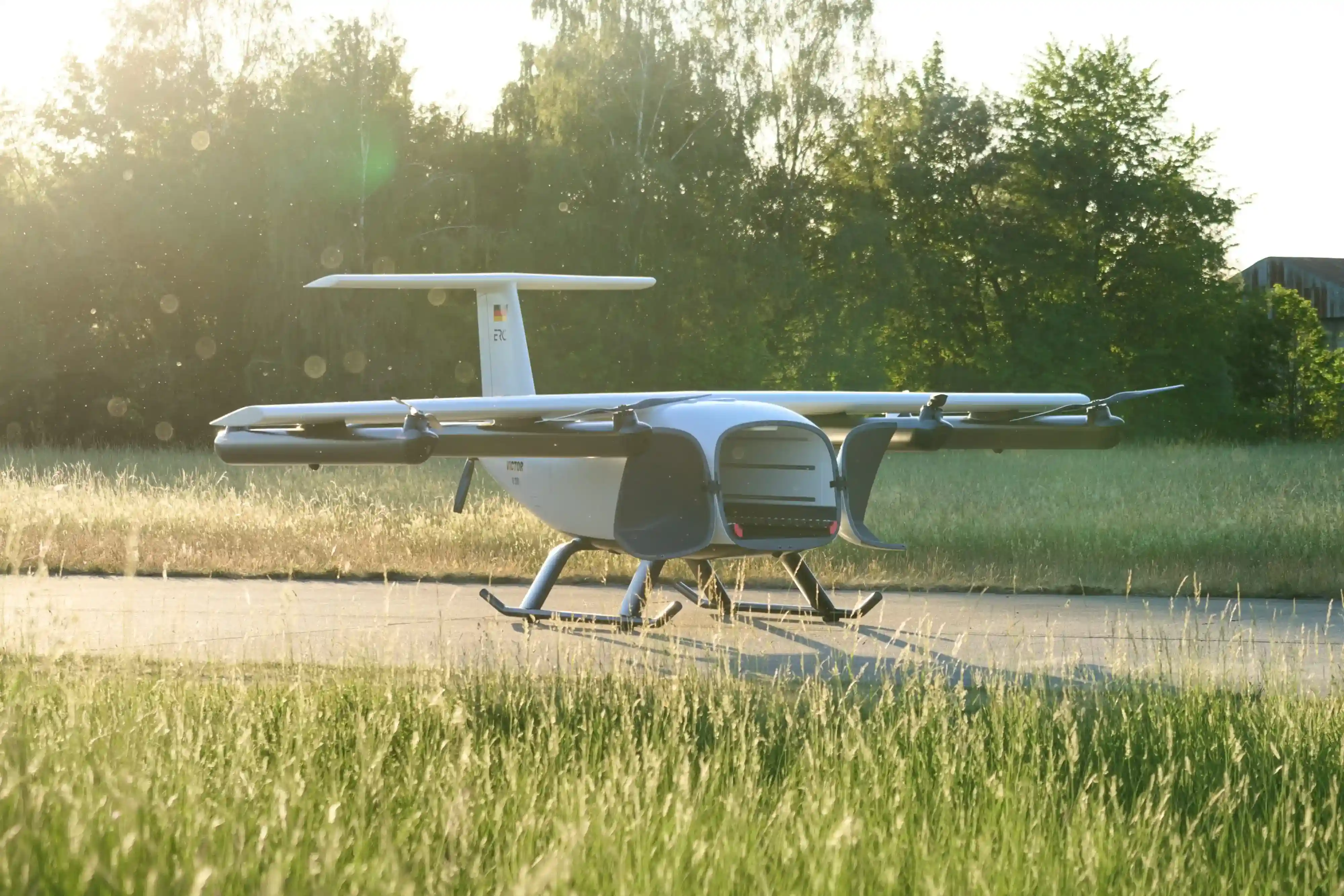 Small drone airplane with open cargo bay on runway in grassy field at sunset.