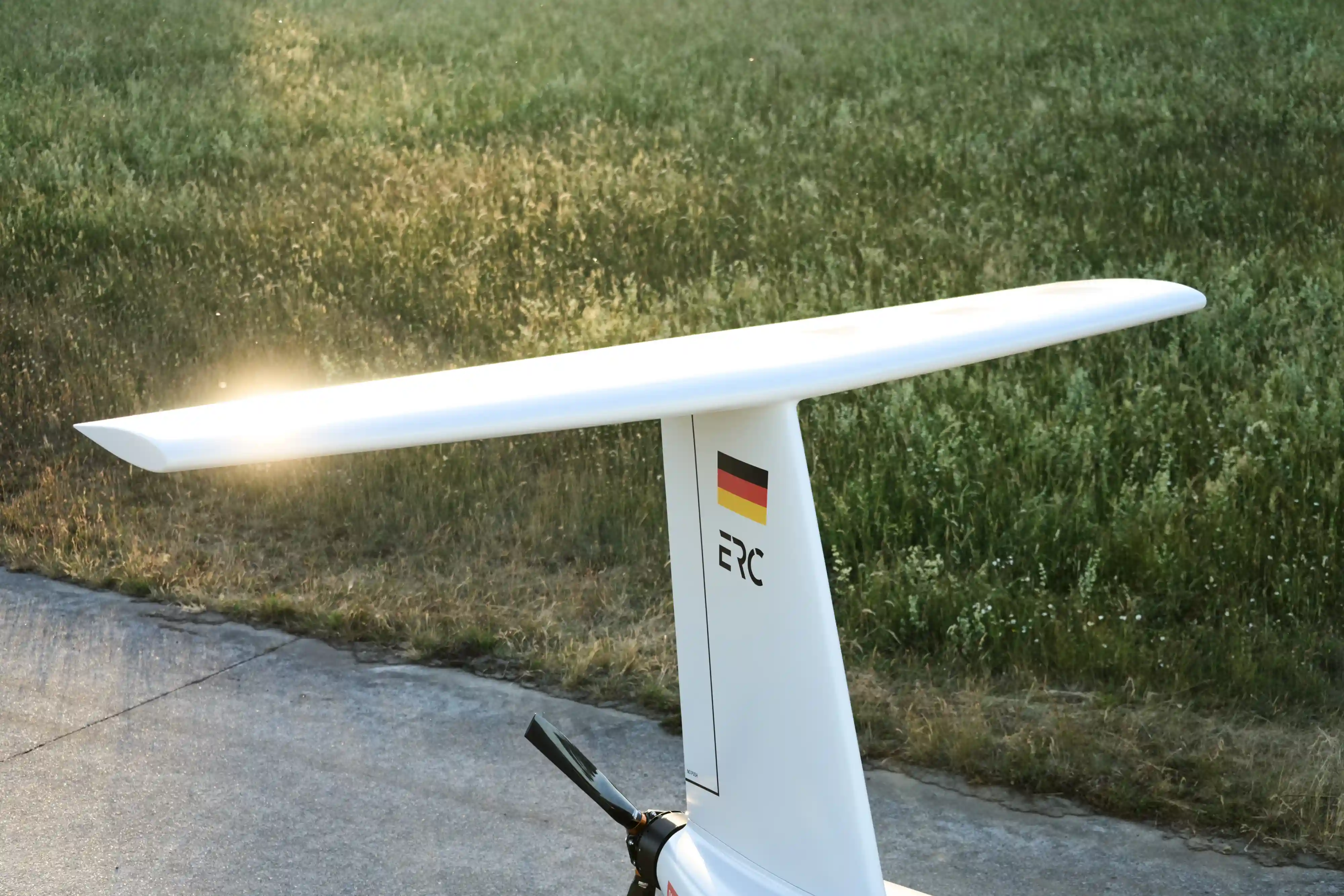 White aircraft tail with a German flag and ERC logo near grassy field and concrete surface.