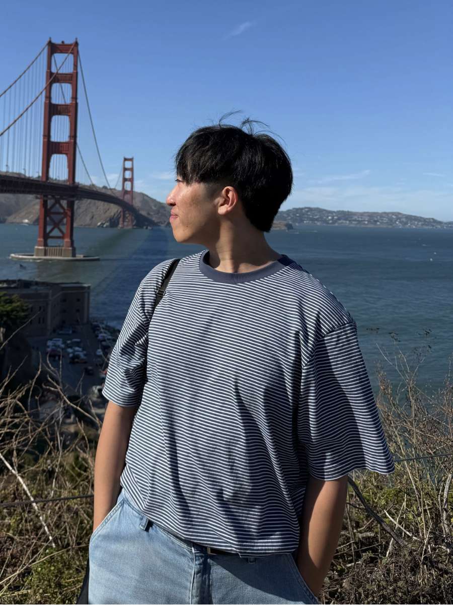 A man looking to his right in the direction of Golden Gate Bridge with the bay behind him and a clear blue sky