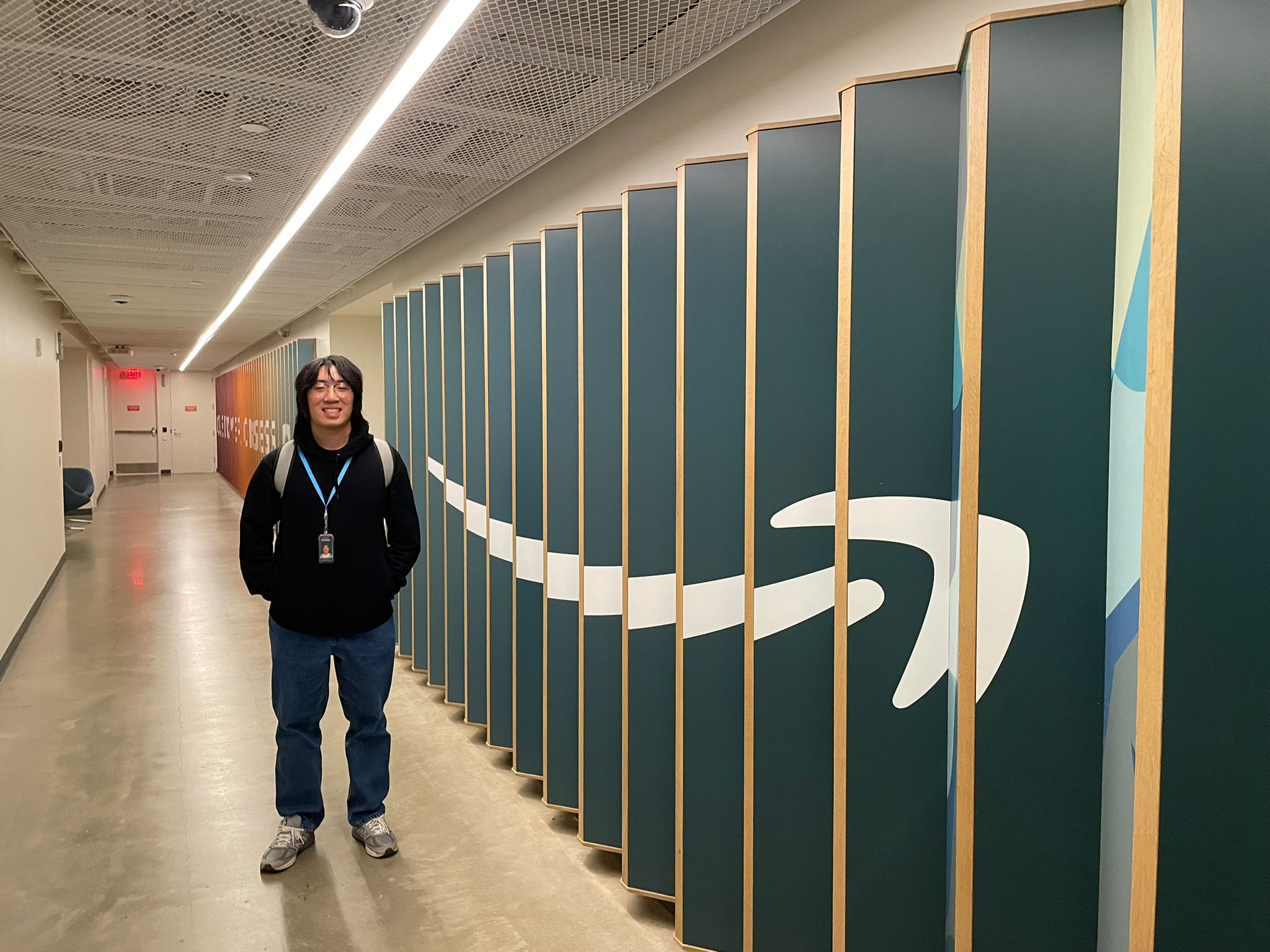 A now former tech employee with glasses stands next to the company logo printed on a jagged wall at one of the company's offices