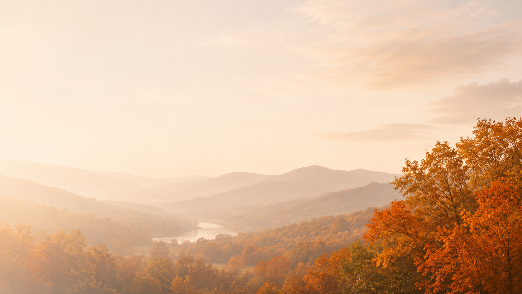 Rolling hills covered with autumn trees in shades of orange and yellow, with a river winding through the valley under a soft, hazy sky at sunrise or sunset.