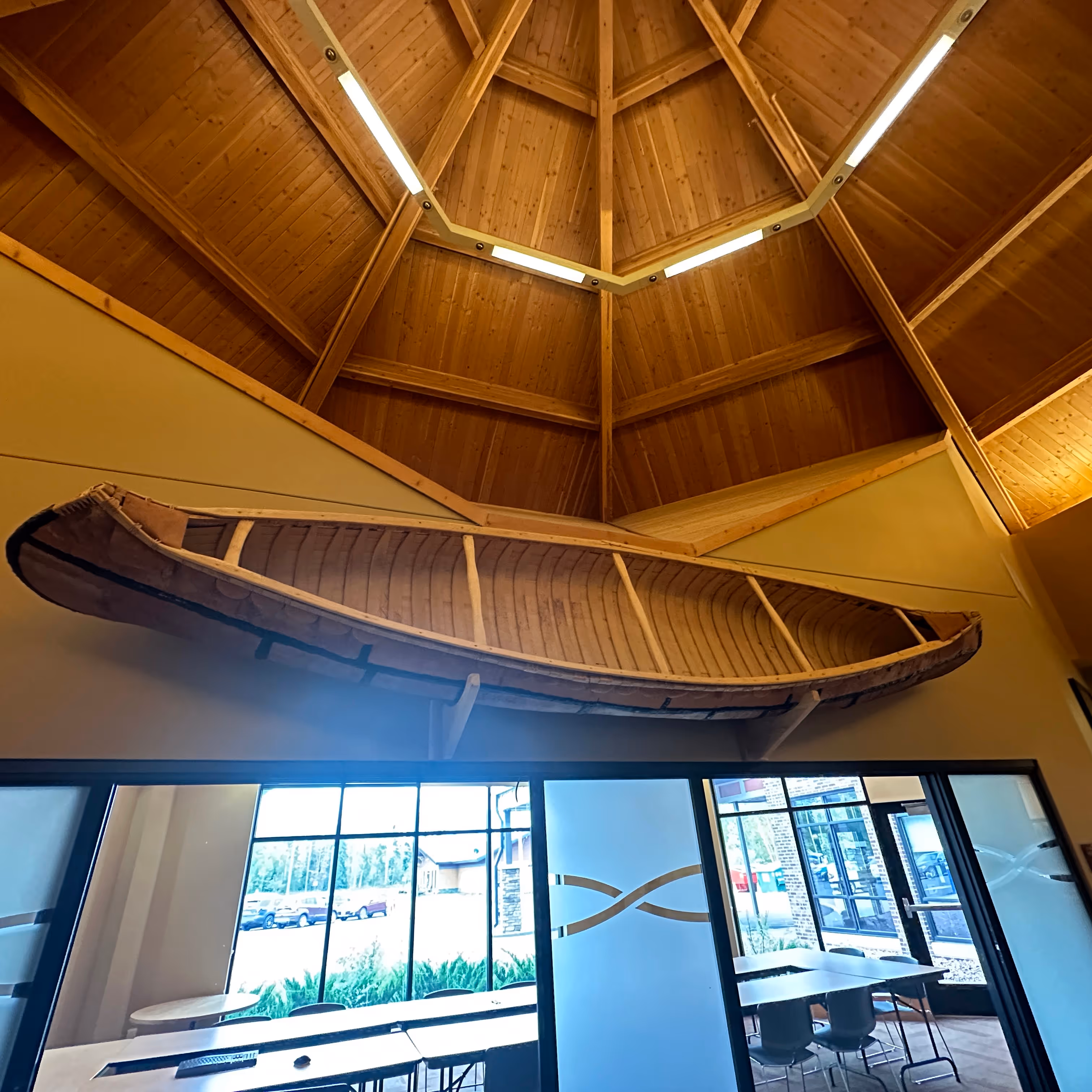 Wooden canoe mounted on wall below a high wooden ceiling with skylights in a modern room.