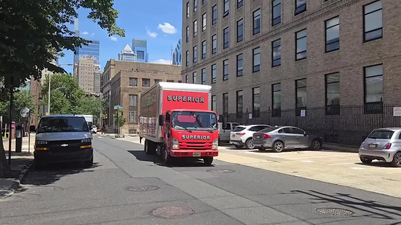 A red Superior moving truck driving through a downtown city street.