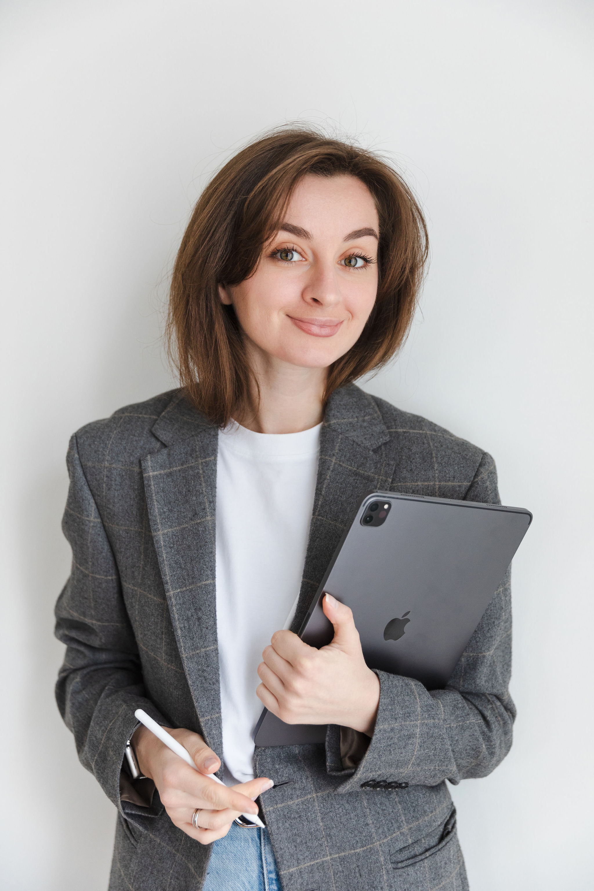 Woman in gray plaid blazer holding an Apple iPad and a stylus, smiling at the camera.