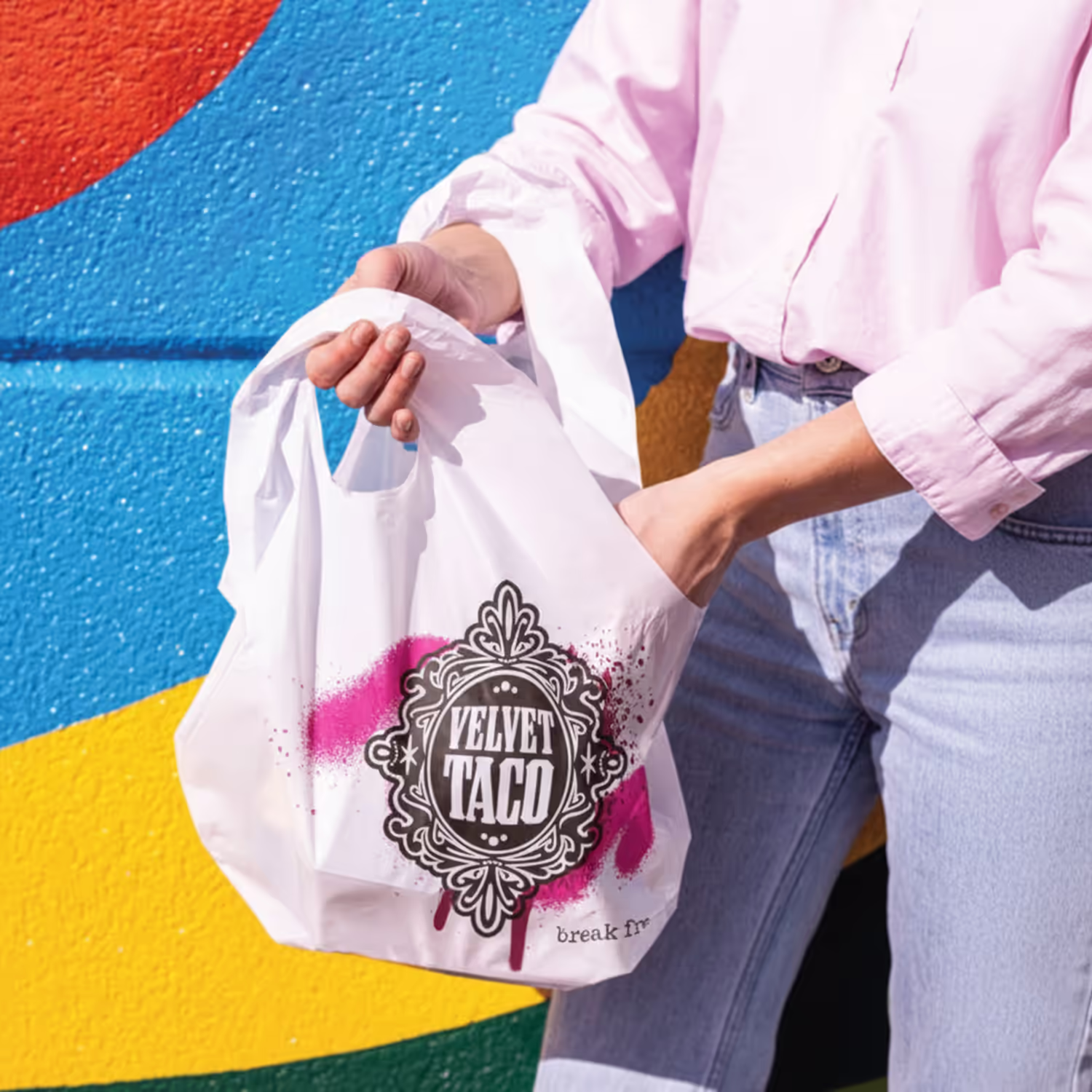 Person holding a Velvet Taco branded tote bag against a vibrant geometric background