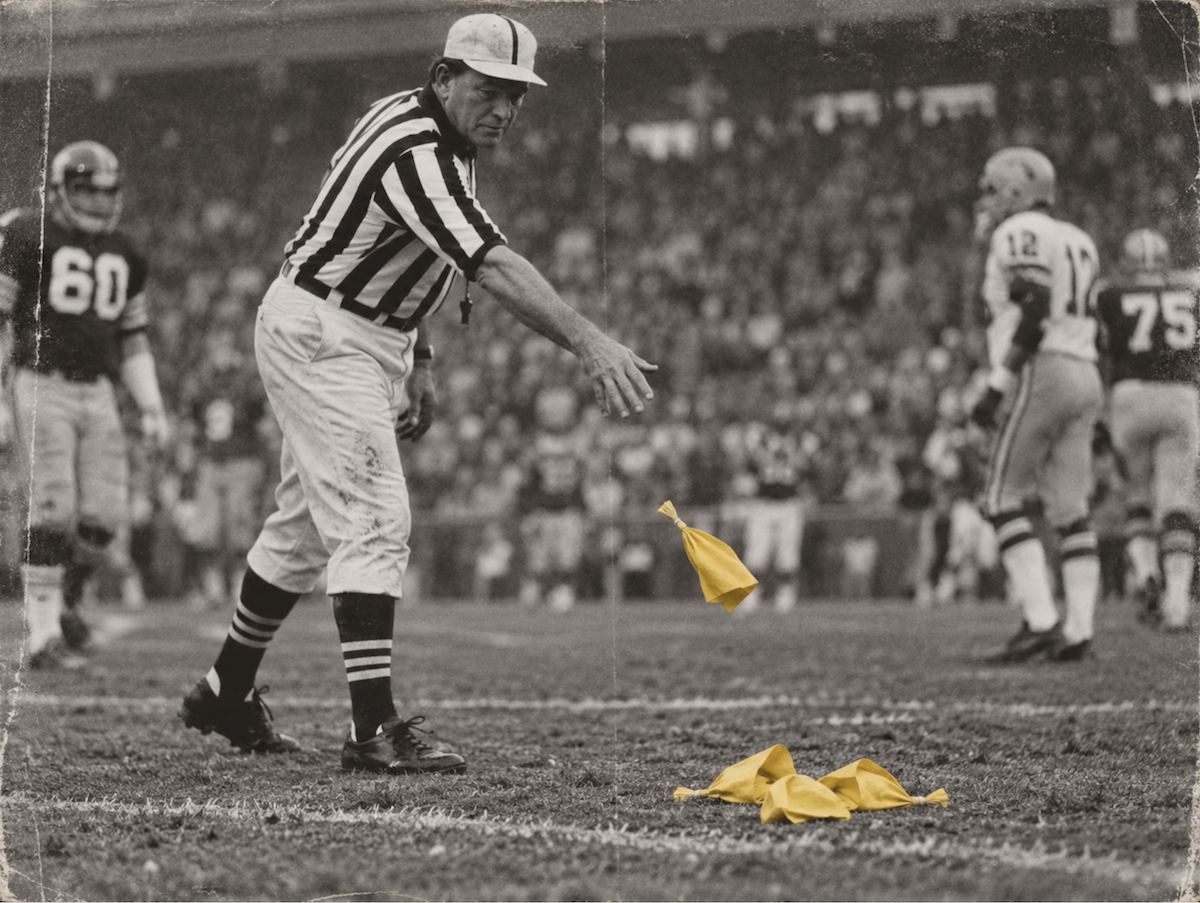 A referee tosses another yellow flag onto a field where flags are already piling up.