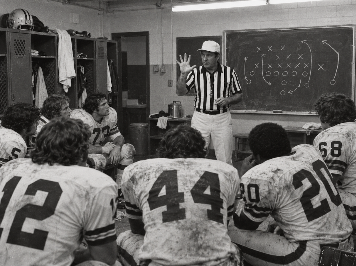 A referee counts to five in front of a locker-room chalkboard.