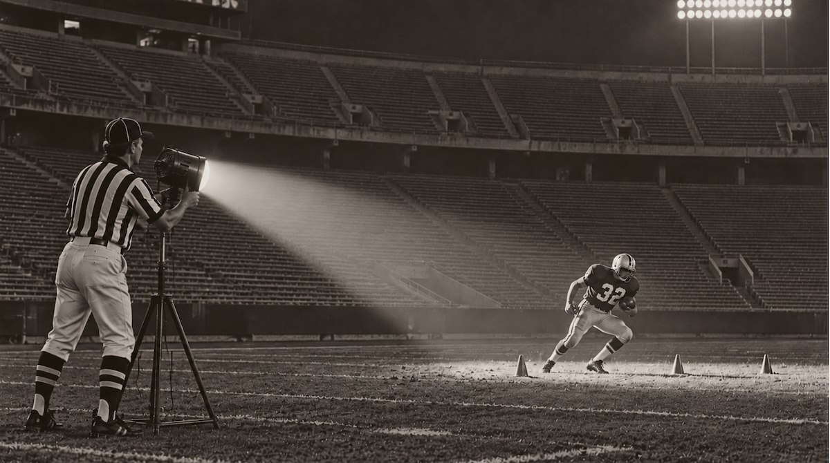 A referee aims a spotlight at a lone player in an empty stadium.